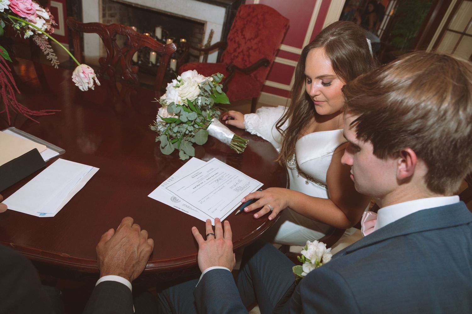 Bride and groom signing official wedding marriage certificate at wooden table.