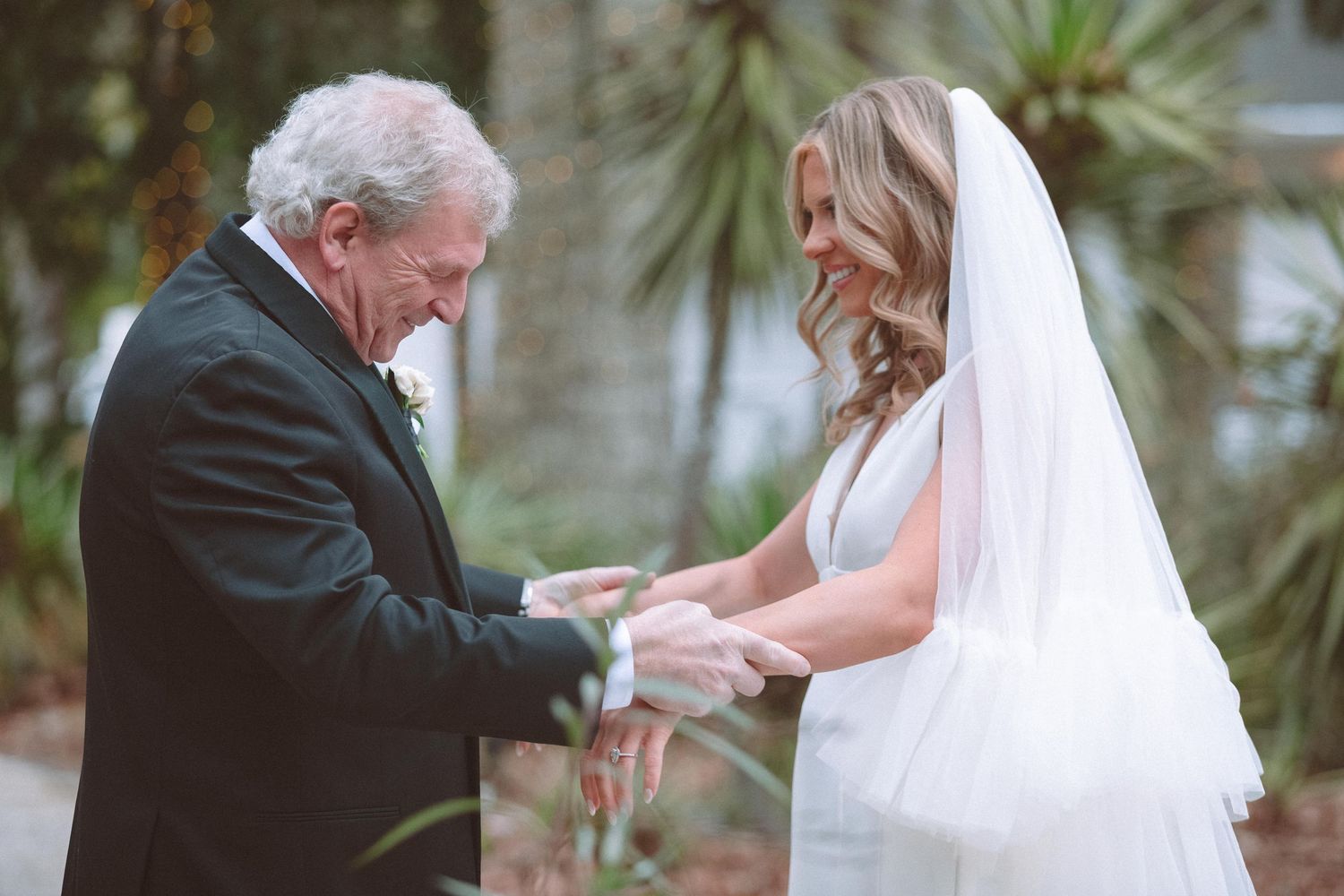 Bride and older gentleman exchanging rings outdoors during wedding ceremony.