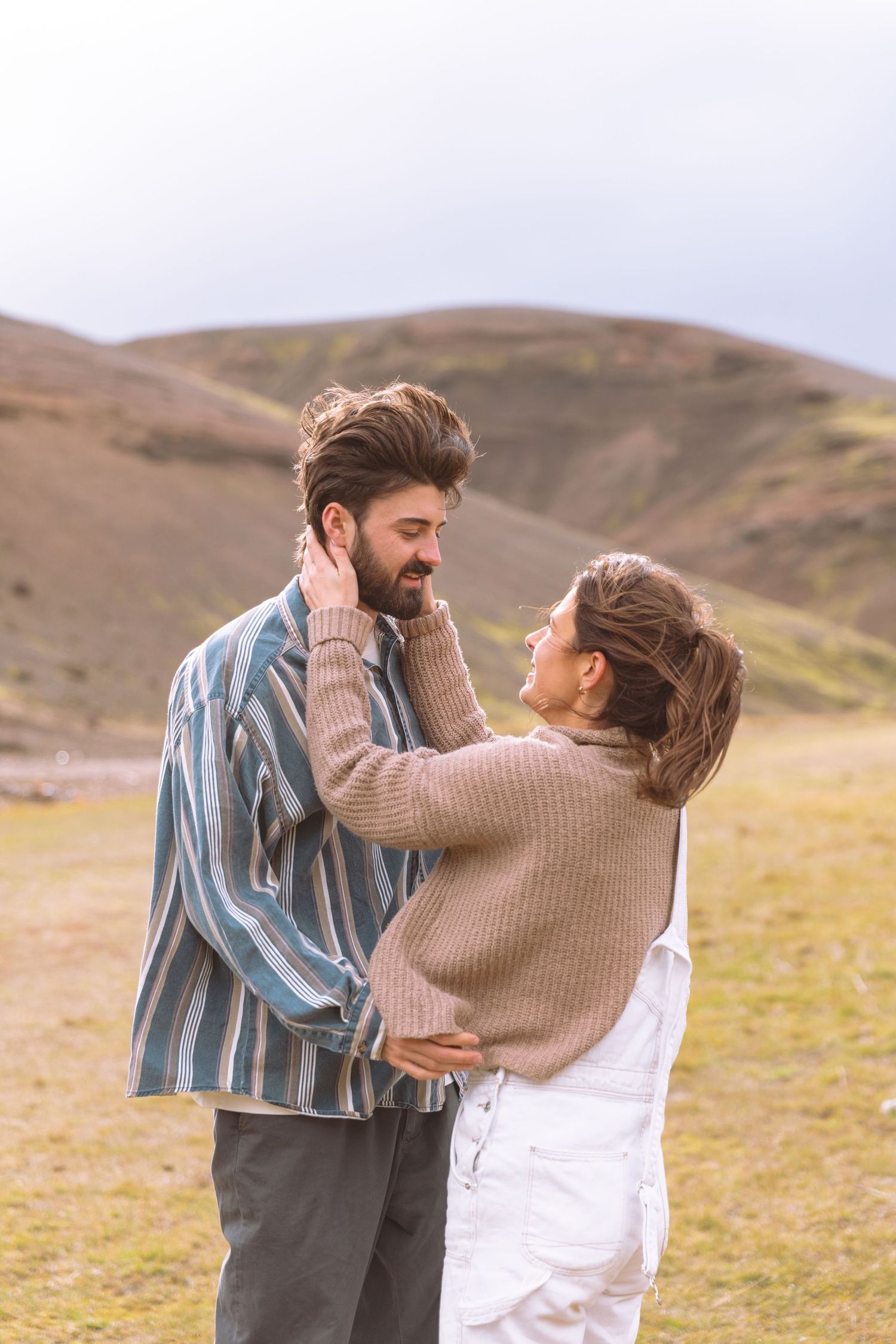 Couple standing face to face in green mountain landscape, woman touching mans face tenderly.