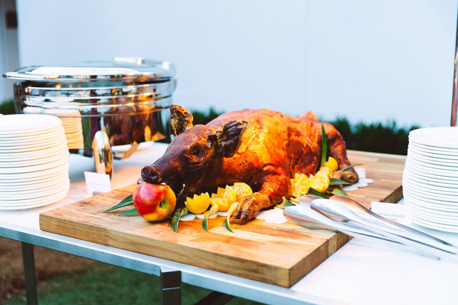 Golden roasted whole turkey on wooden board with apples and oranges at buffet table.