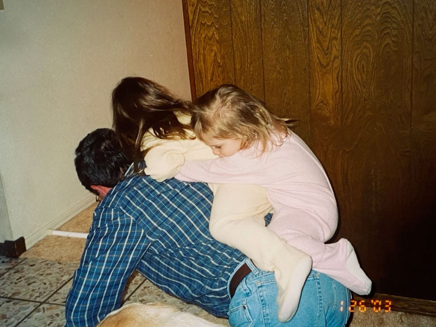 A man crouching on the floor while two young girls climb on his back in a playful moment.