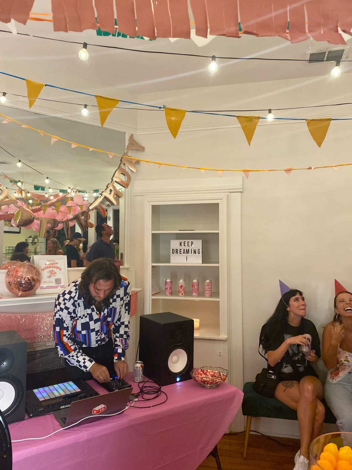 DJ performing at a festive indoor party with colorful bunting, string lights, and disco ball decorations.