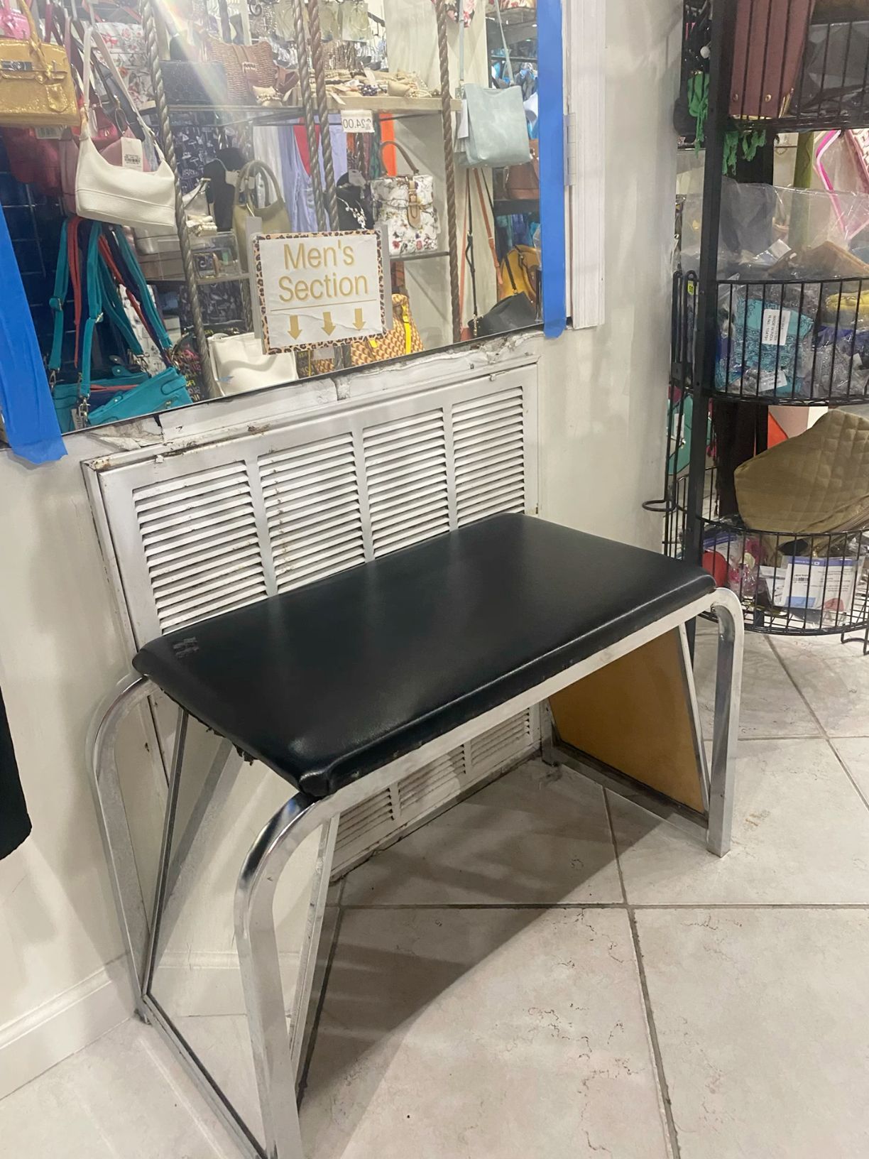 Black top chrome frame desk with sleek modern design displayed in a thrift store near a Men's Section sign.