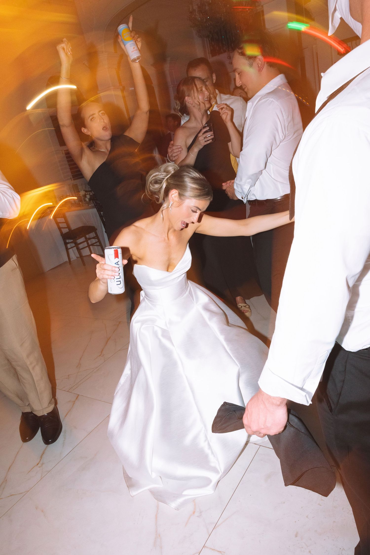 Bride in white gown holds a can while dancing energetically on the wedding reception dance floor.