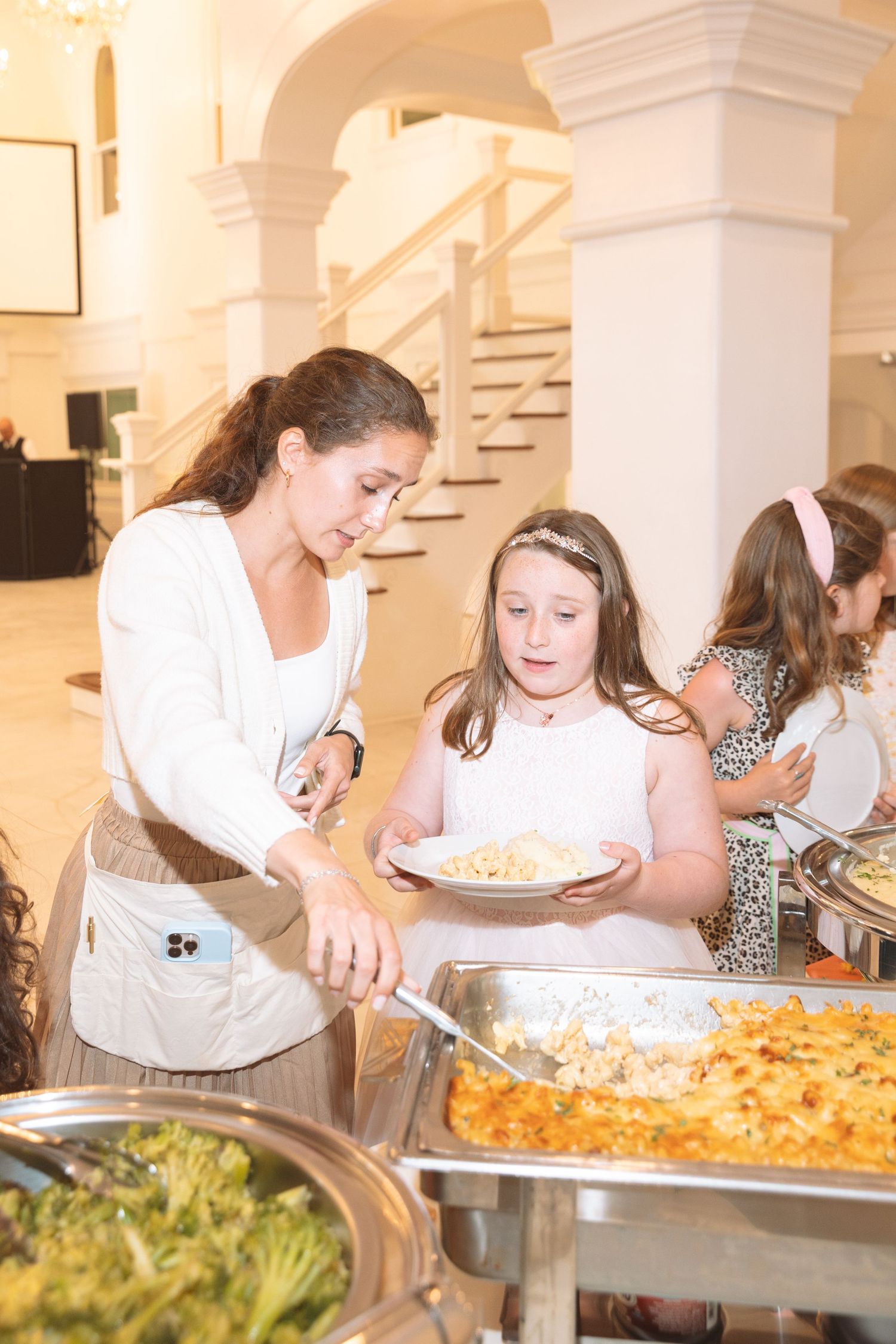 Woman serving food to a young girl at an elegant buffet spread in a formal venue.