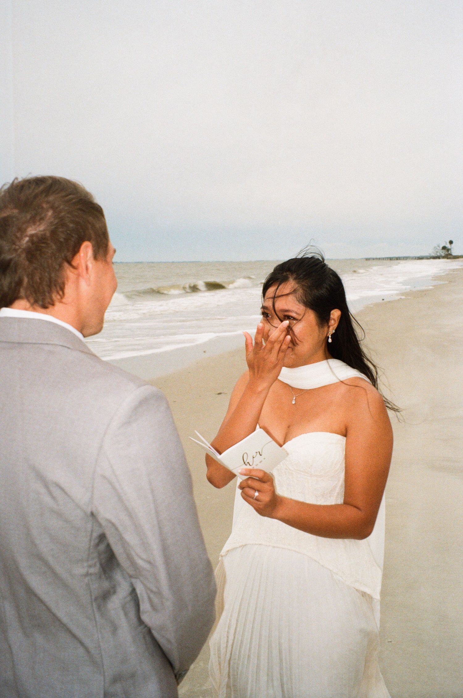 Bride crying happy tears while reading vows to groom during romantic beach wedding ceremony.