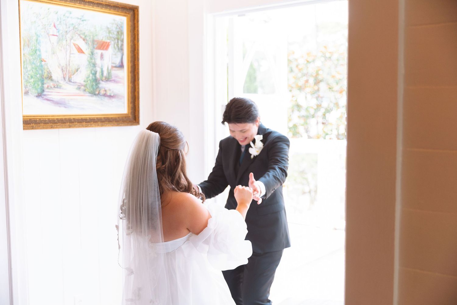 Bride and groom share a tender first look moment in a sunlit doorway before their wedding ceremony.