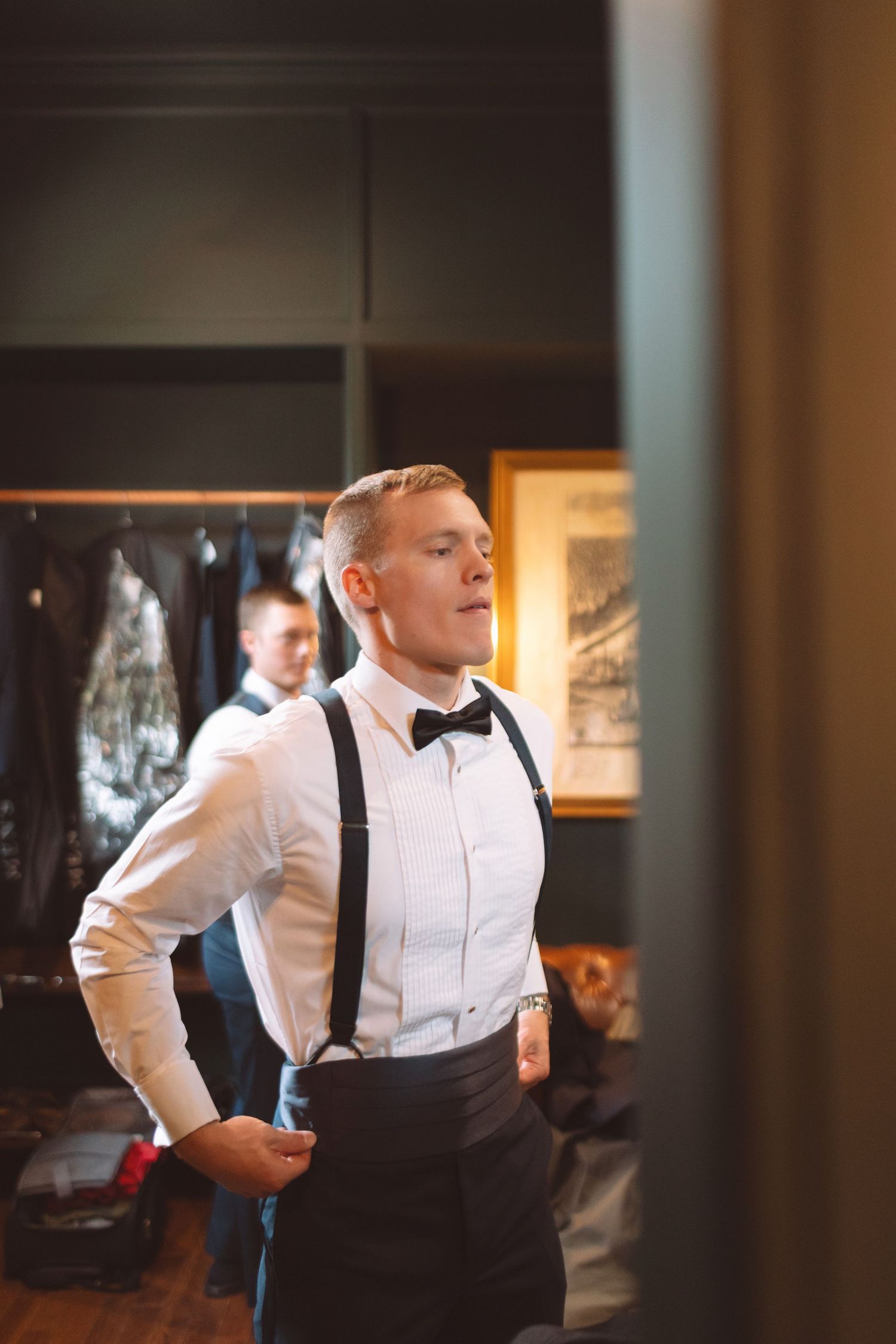 Groom getting dressed in suspenders and bow tie before wedding ceremony.