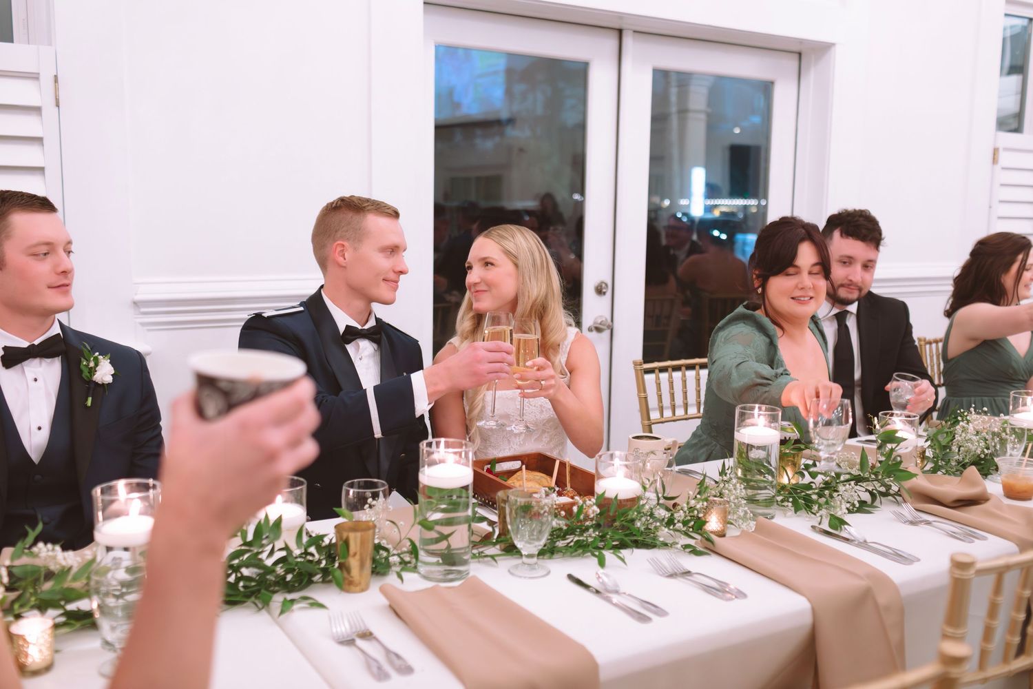 Wedding reception guests raising glasses for a toast at an elegantly decorated dining table.