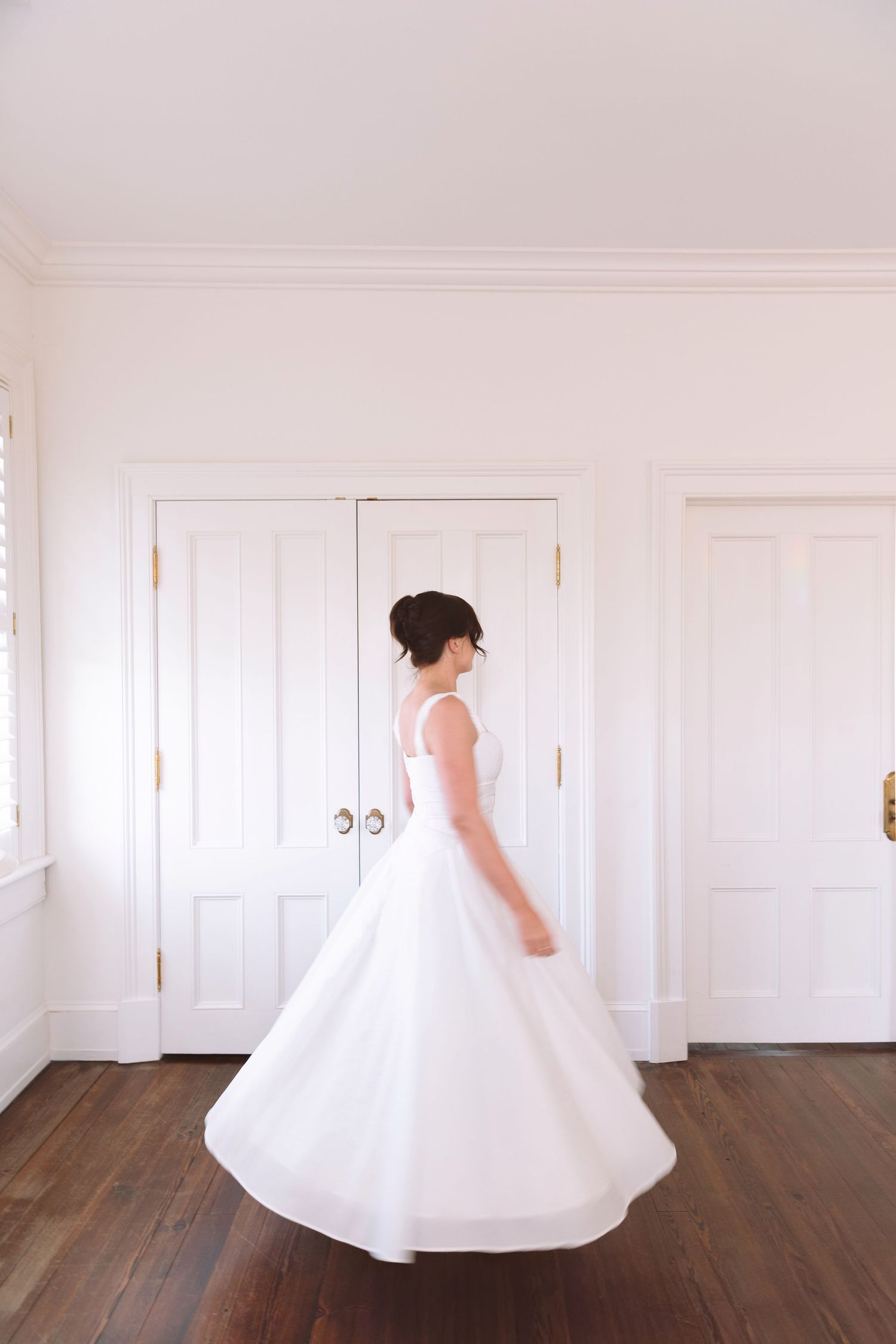 Bride in classic white ball gown twirls gracefully in bright white interior room.
