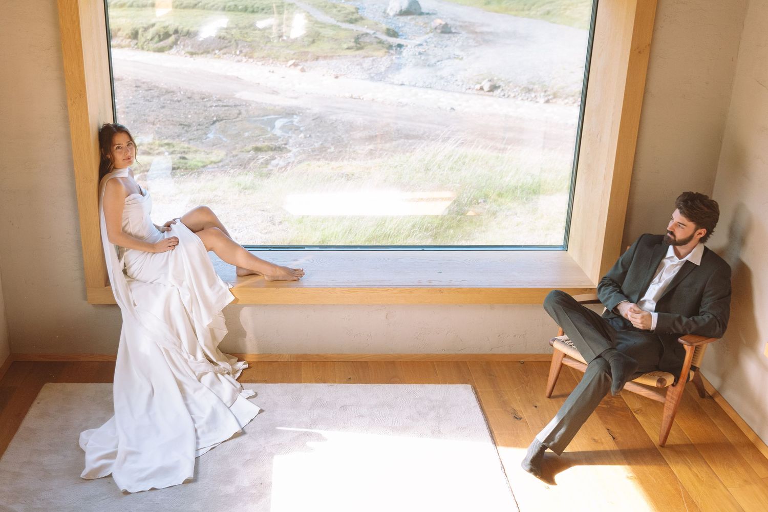 Bride and groom relaxing by a large window with scenic outdoor construction views.