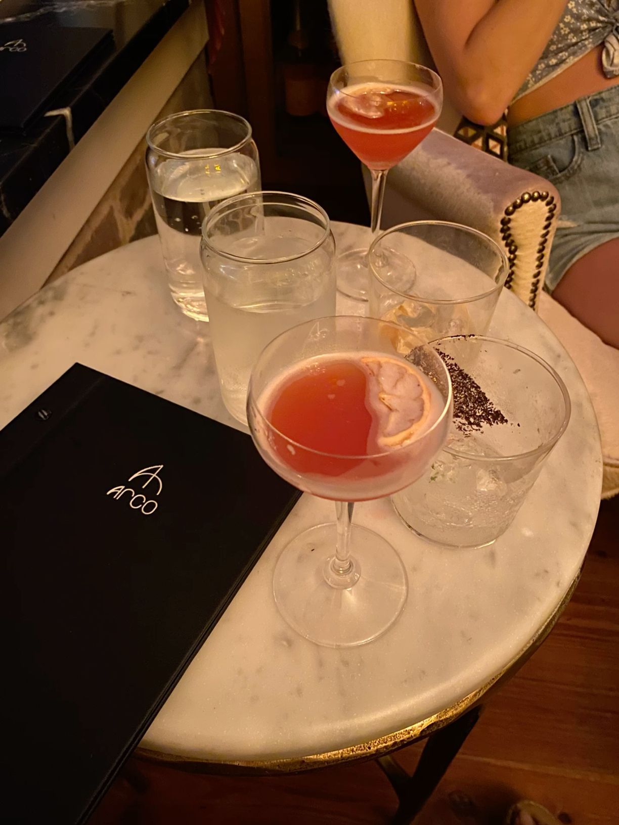Pink cocktails and drinks on a marble table next to a restaurant menu.