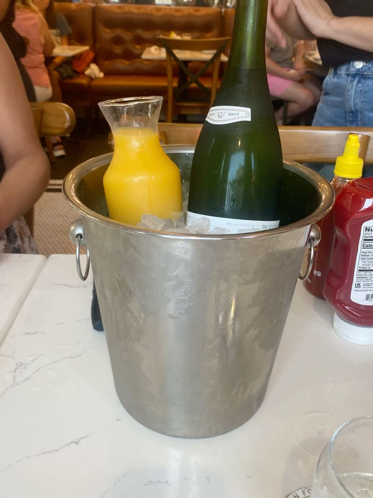 Champagne bottle and orange juice carafe chilling in an ice bucket for brunch mimosas.