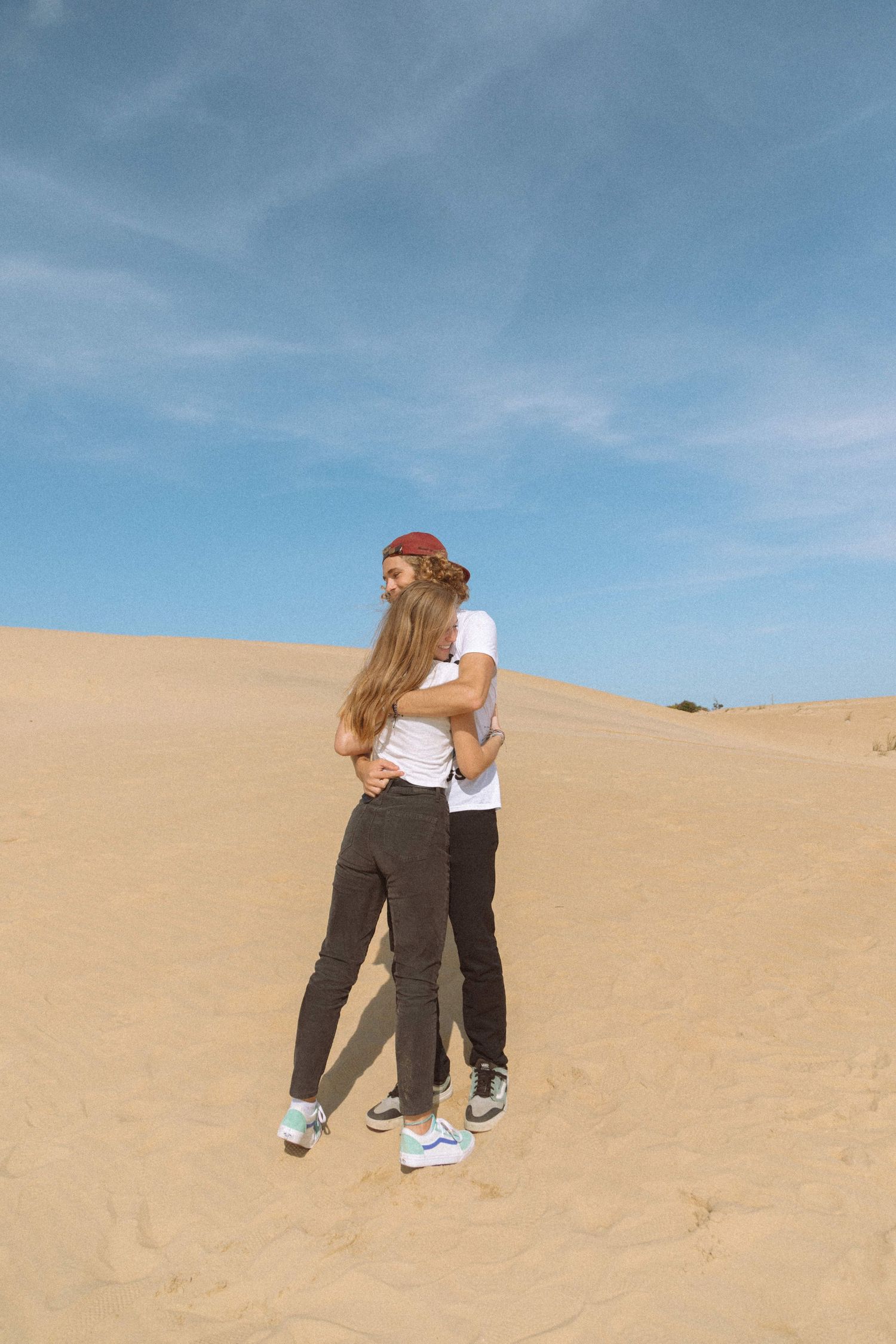 Young couple embracing on a sandy desert dune under a bright blue sky.