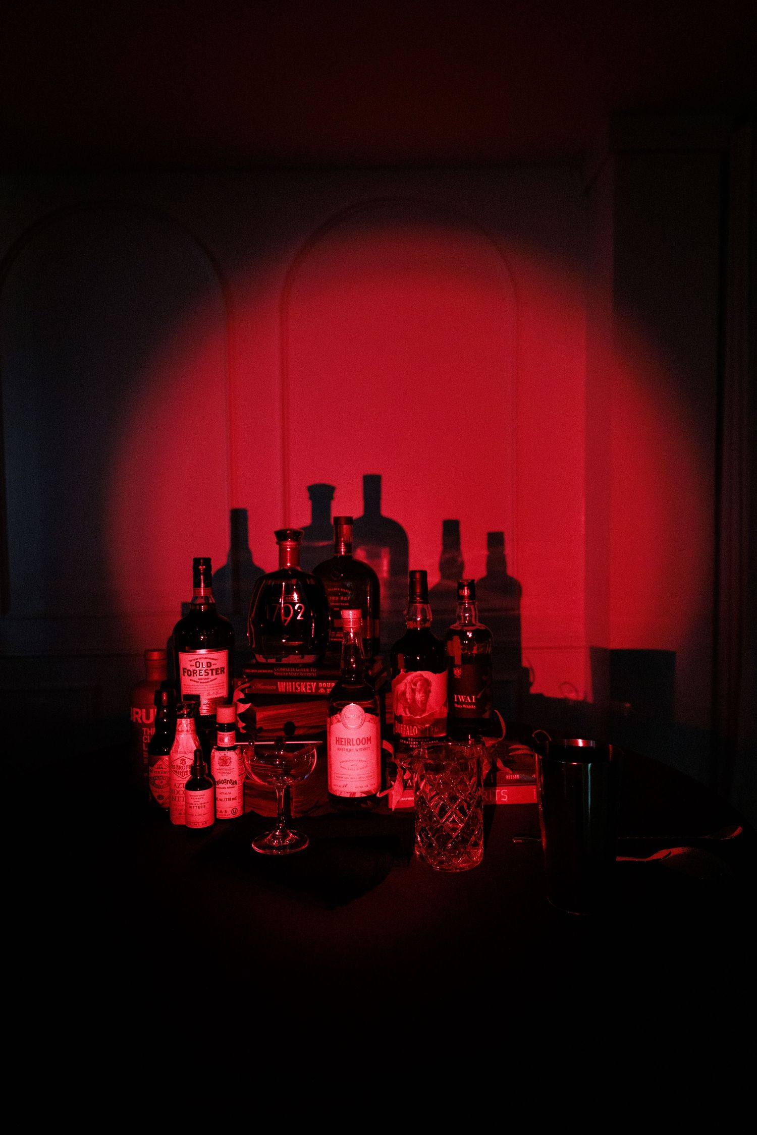 Moody bar setup with liquor bottles illuminated by dramatic red lighting against a dark background.