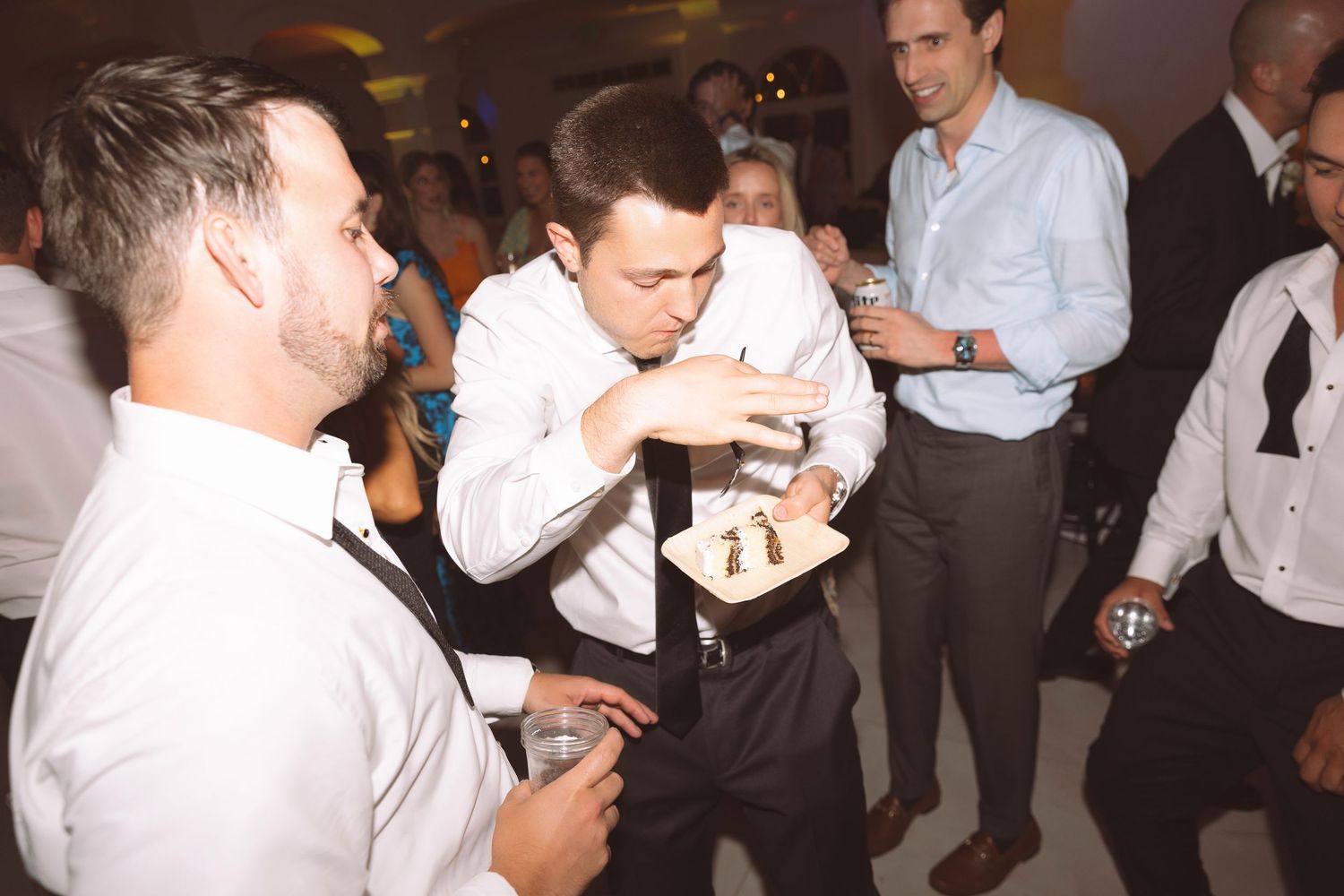 Men in white shirts socializing at a lively indoor party event on a dance floor.