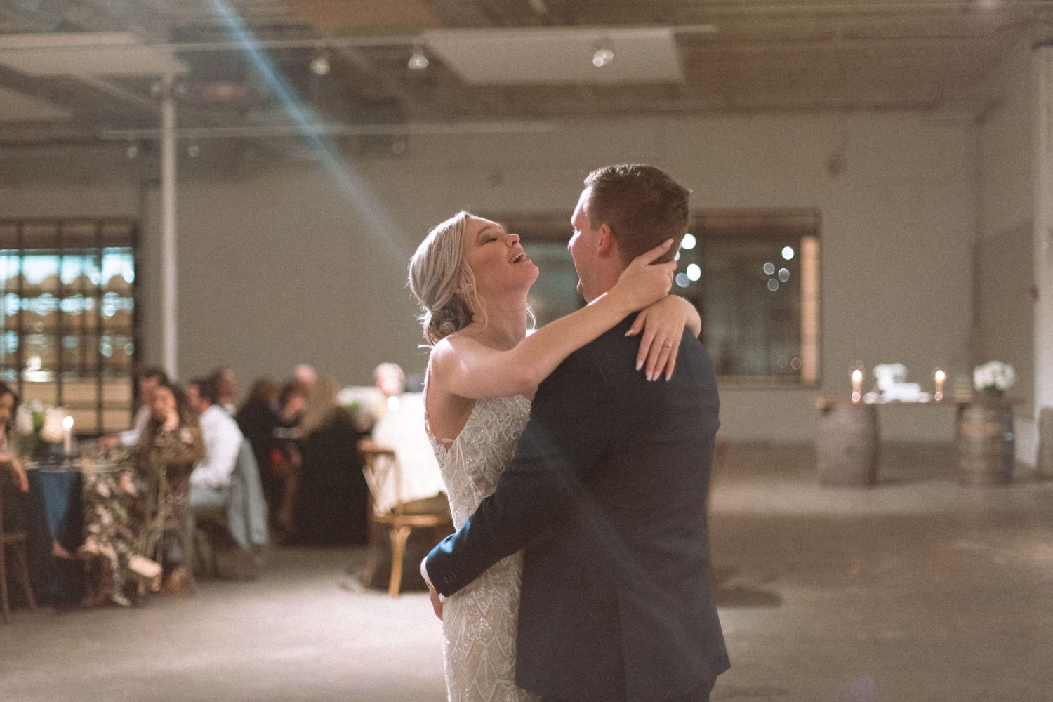 Bride and groom share emotional first dance in softly lit rustic wedding venue.
