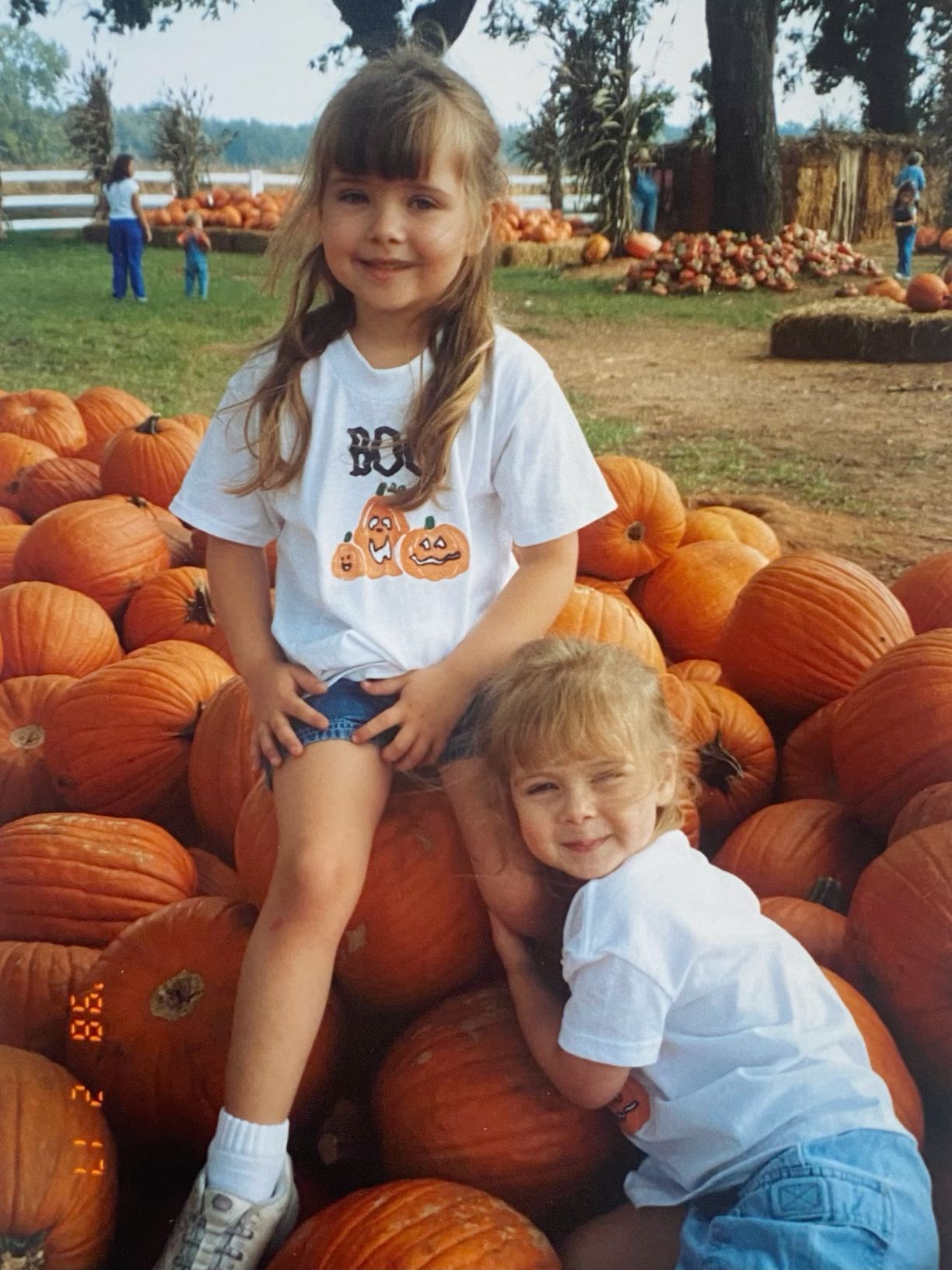 Two young sisters posing among pumpkins at a fall pumpkin patch.