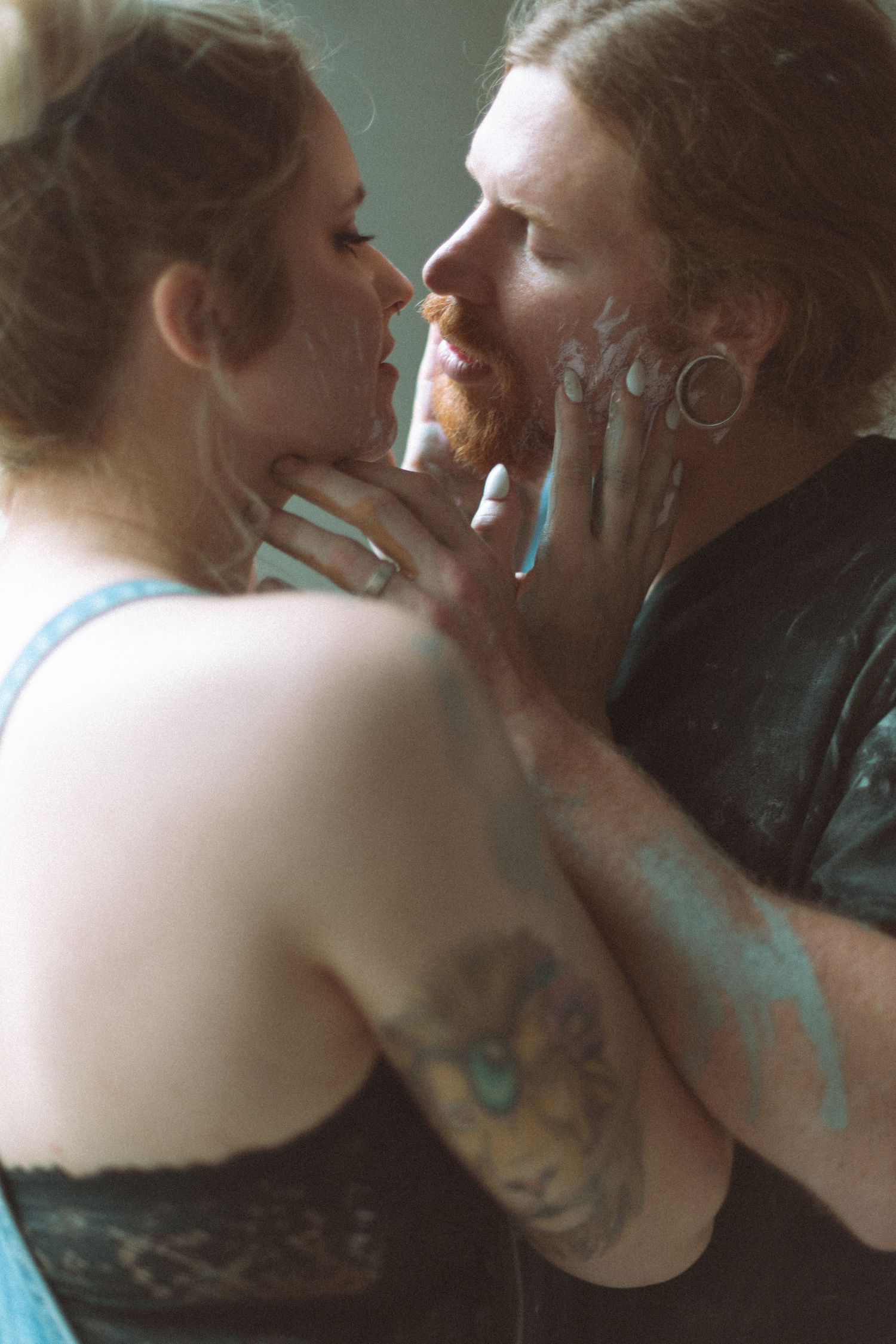 Tattooed couple sharing an intimate moment with blue paint on their faces indoors.
