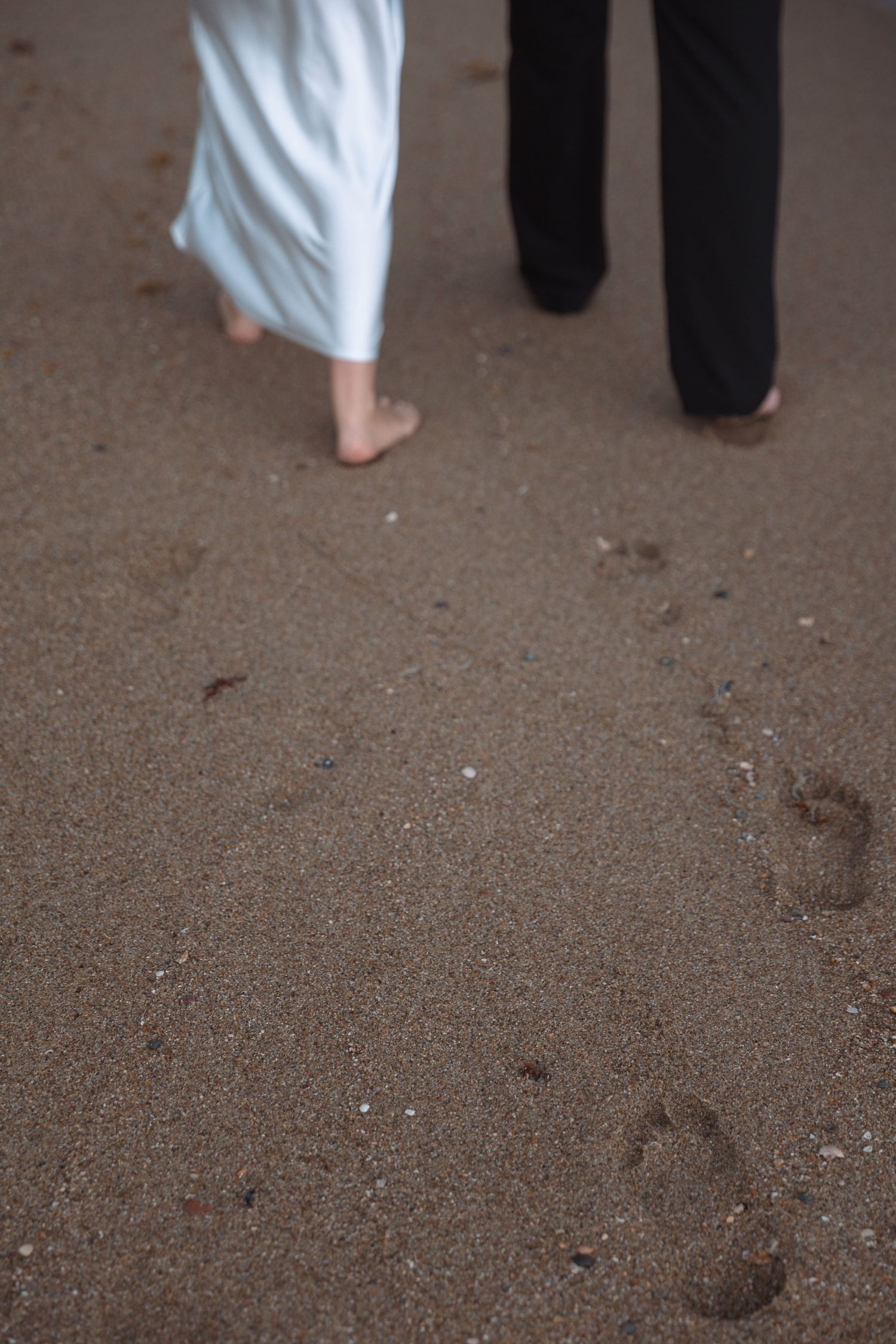 Barefoot couple walking on wet sand leaving footprints on the beach.
