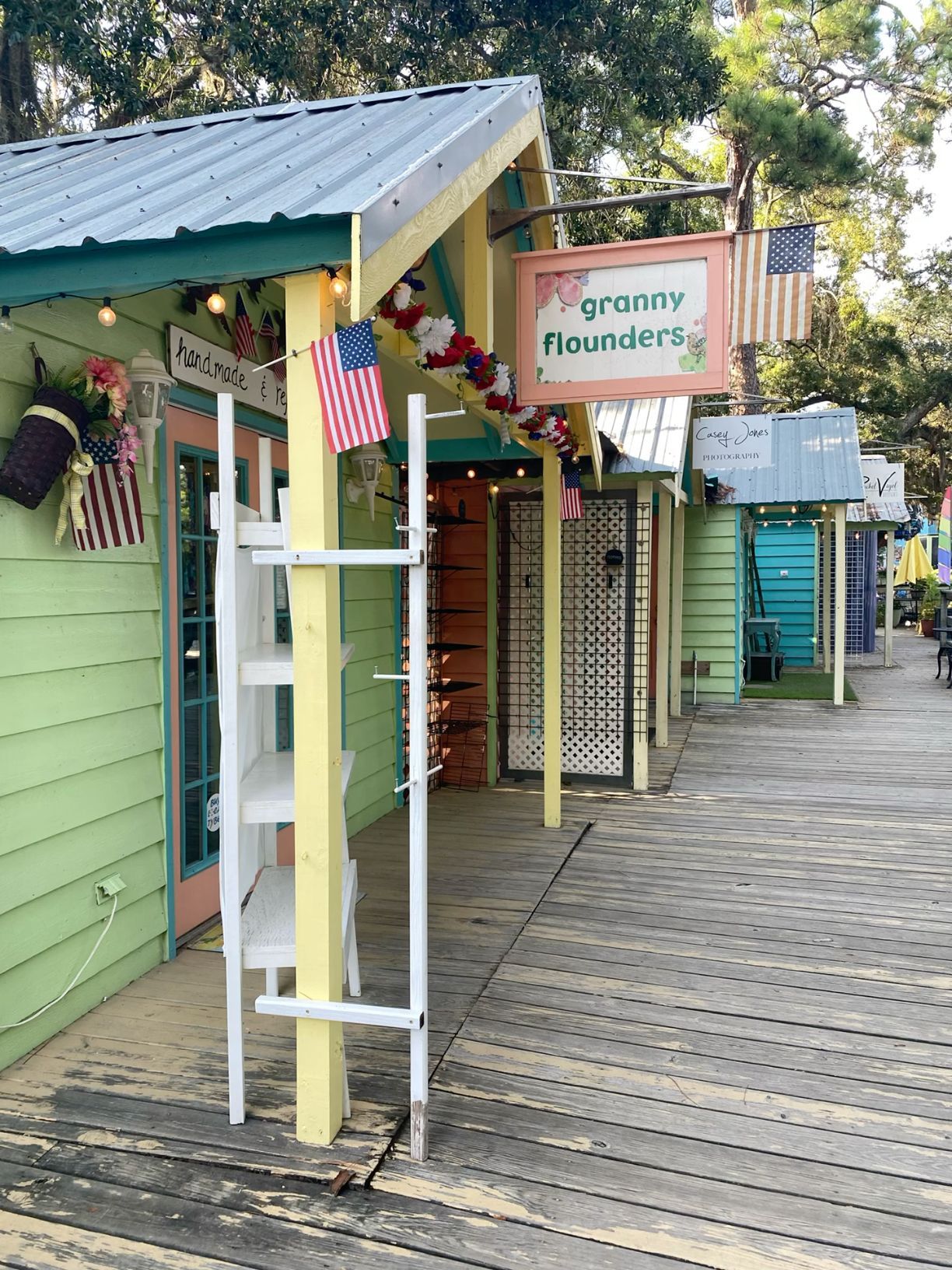Charming wooden boardwalk shops with colorful siding, American flags, and a Granny Flounders sign.