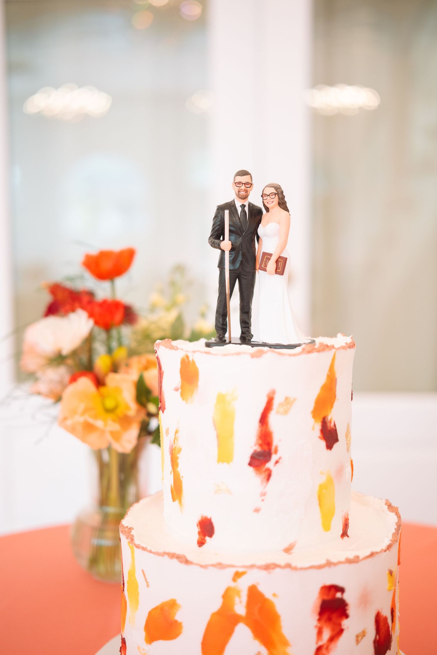 Two-tier white wedding cake with colorful brushstroke design and custom bride and groom cake toppers.