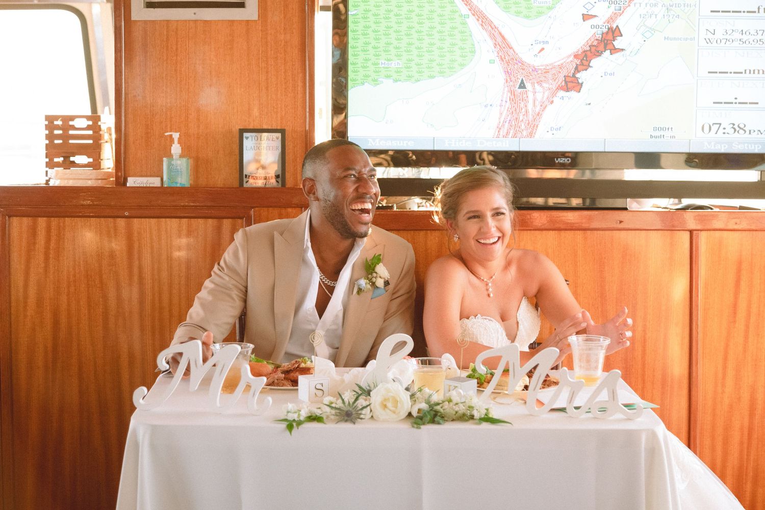 Happy newlywed couple smiling at their sweetheart table decorated with Mr and Mrs signs at a boat wedding.