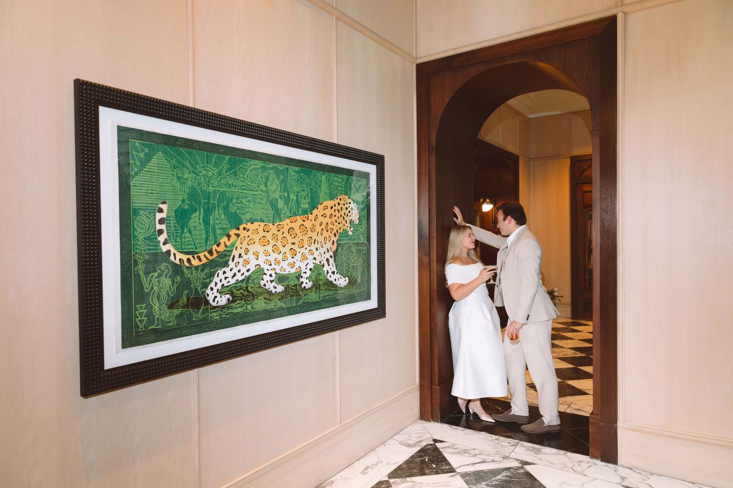 Couple embracing in elegant hallway beside framed leopard artwork during wedding day.