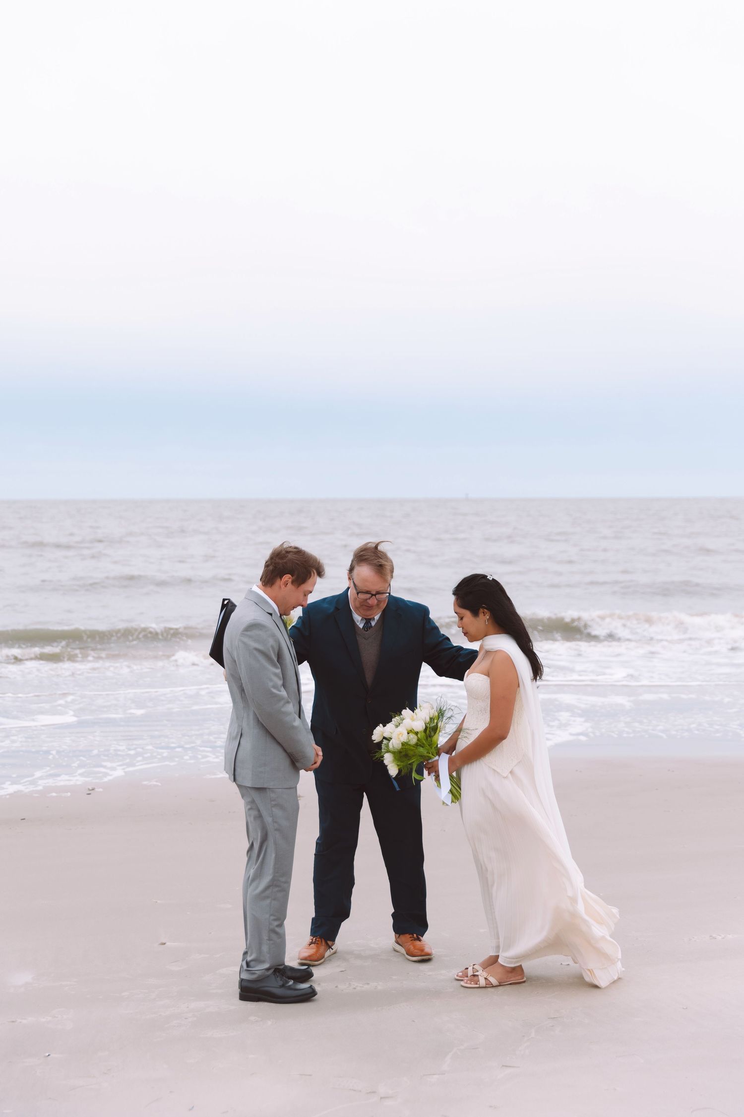 Beach wedding ceremony with couple exchanging vows before officiant at ocean shoreline.