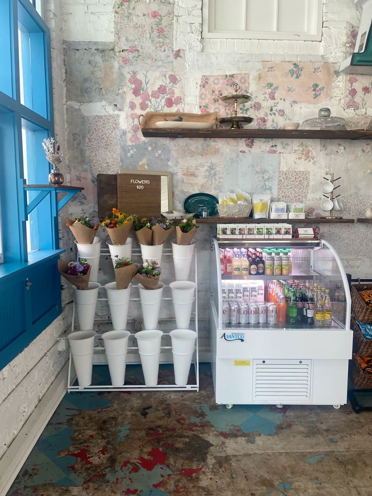 Charming flower shop interior with cone-shaped floral displays, refrigerated beverage case, and vintage floral wallpaper.