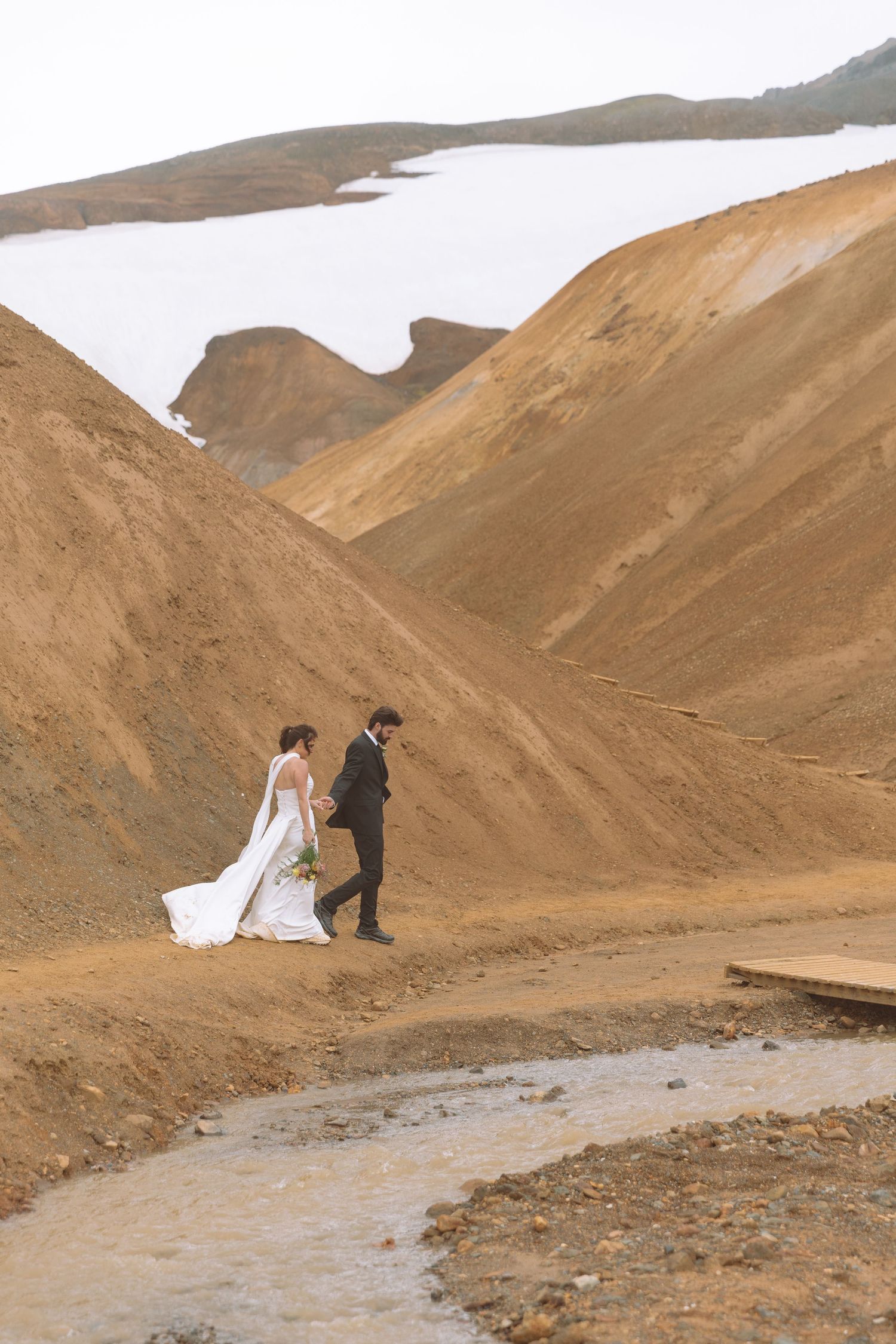 Bride and groom walk hand in hand through a dramatic golden volcanic landscape in Iceland highlands.