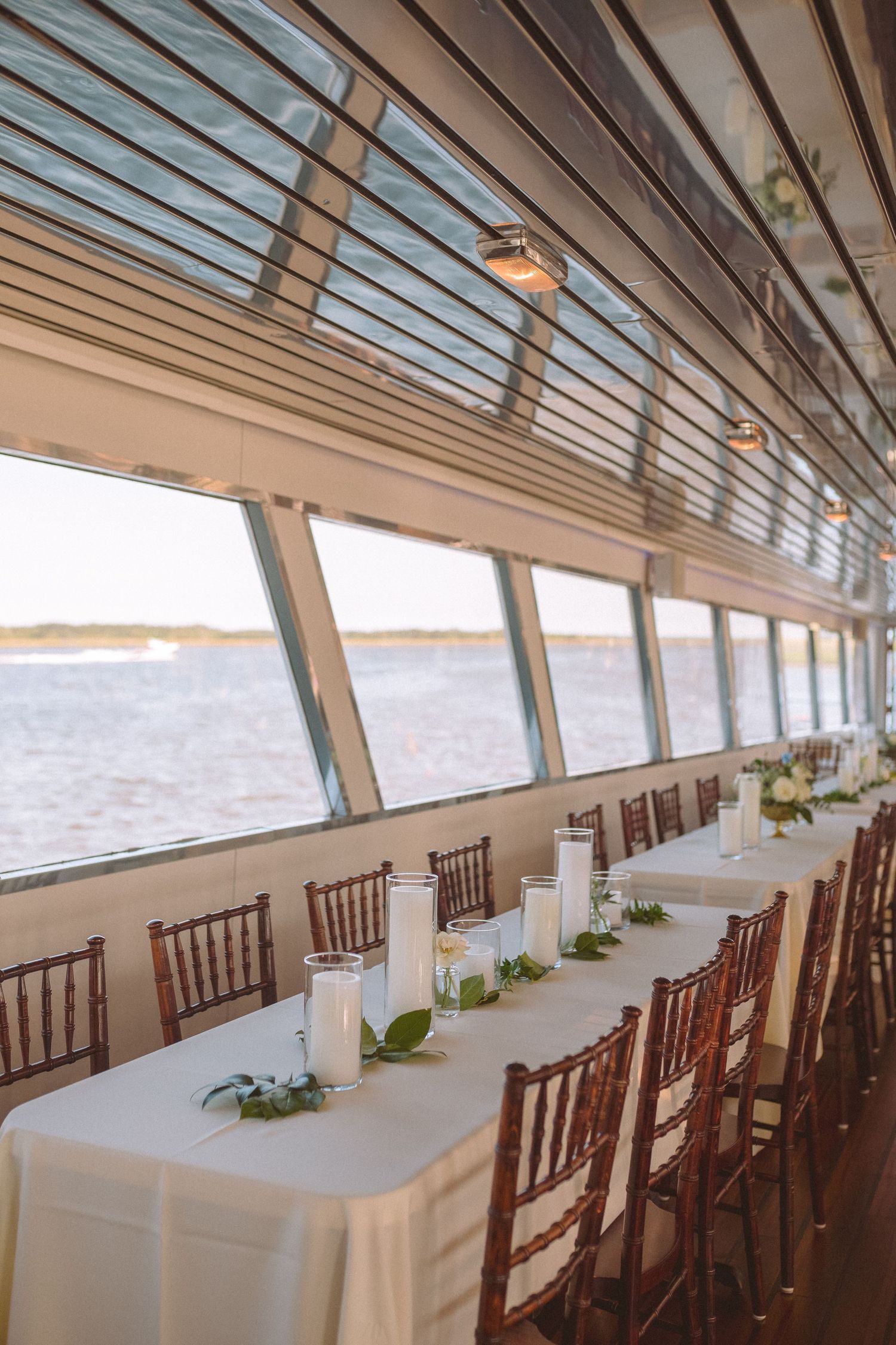 Elegant wedding reception table set on a boat with white linens, candles, and waterfront views.