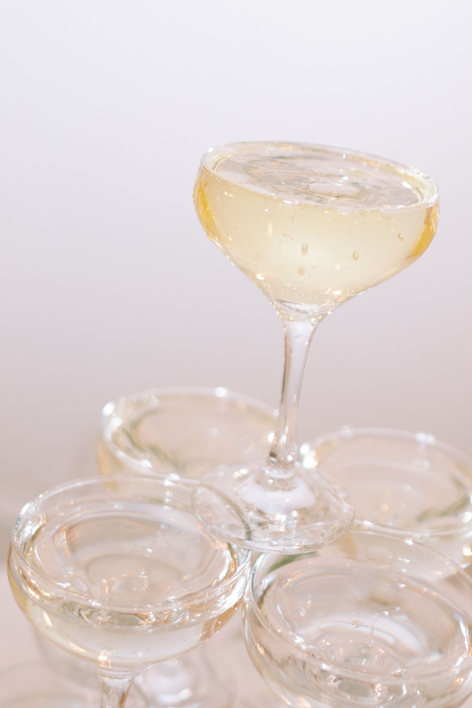 Close-up of a champagne coupe filled with sparkling wine balanced atop a pyramid of glasses.