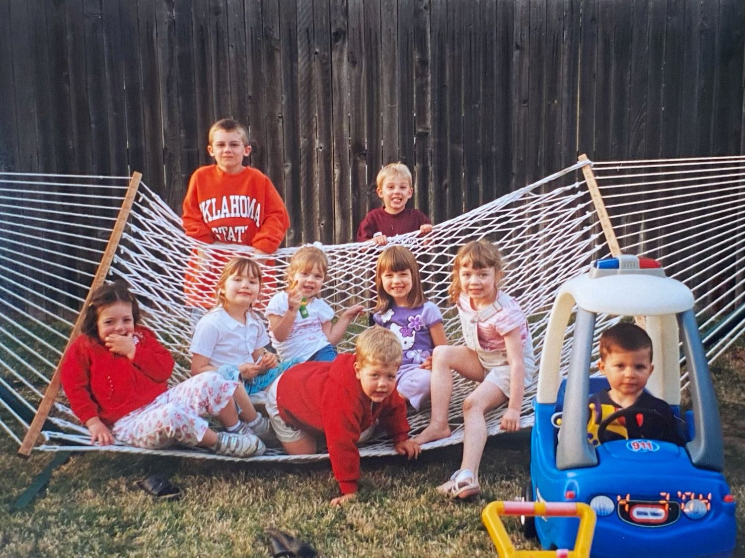 Group of children playing and posing together on a rope hammock in backyard.