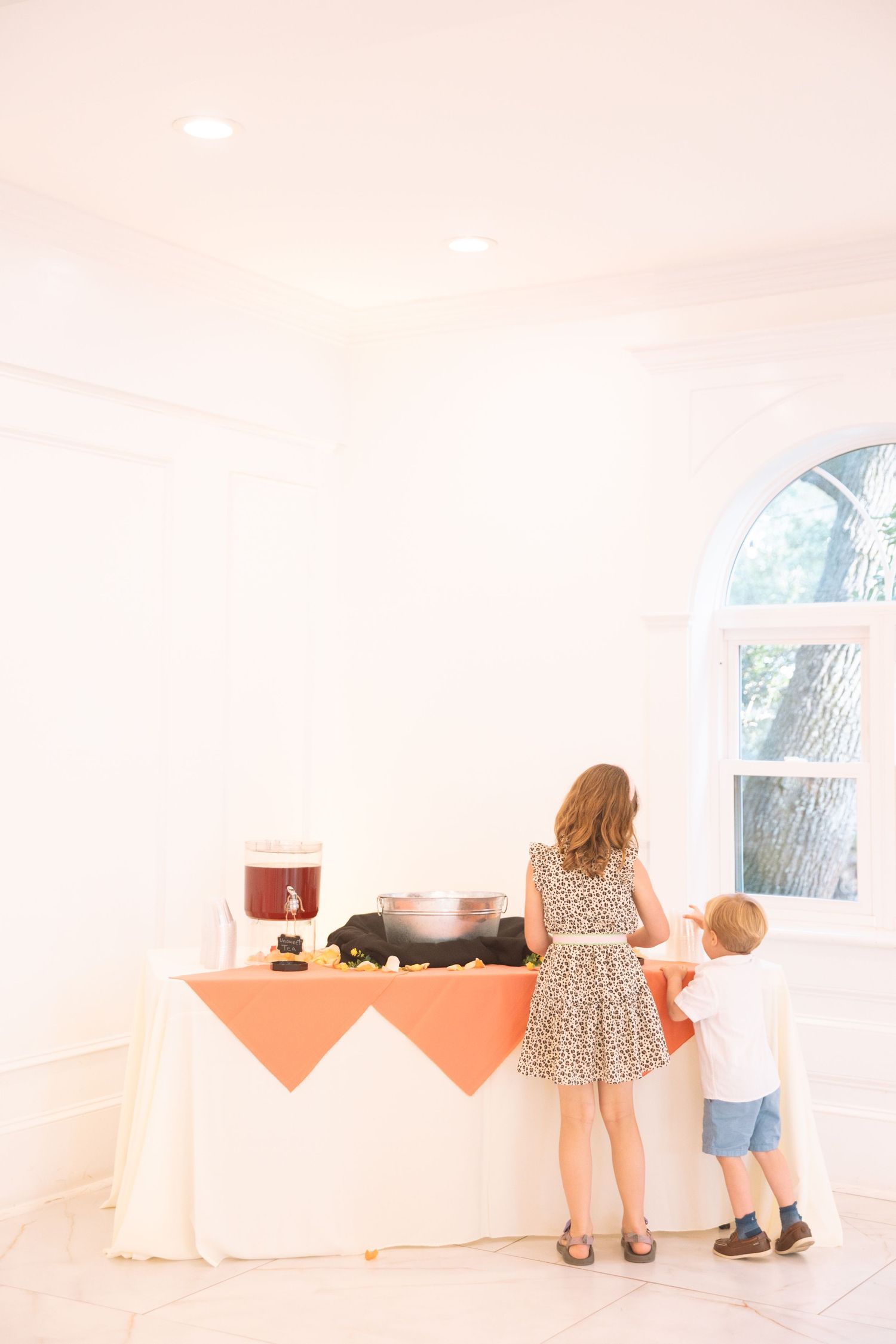 Woman and child standing at a decorated table with orange tablecloth at an indoor event.