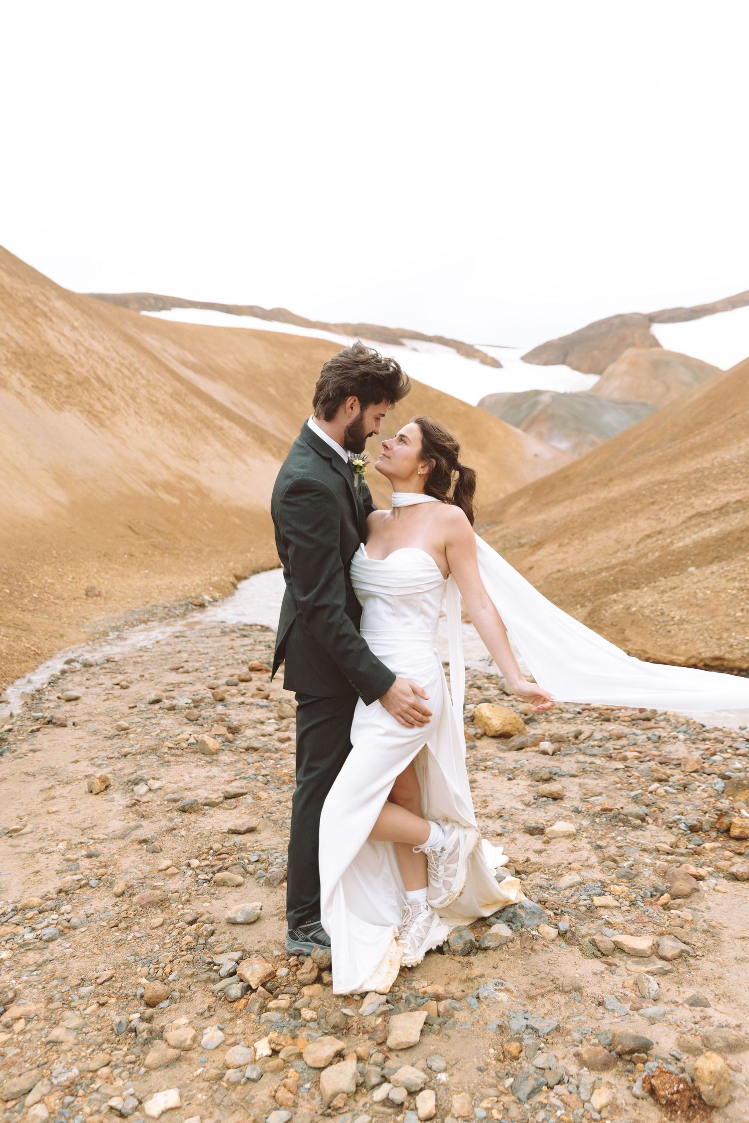 Couple shares a romantic almost-kiss moment outdoors on rocky terrain with sweeping mountain valley views.