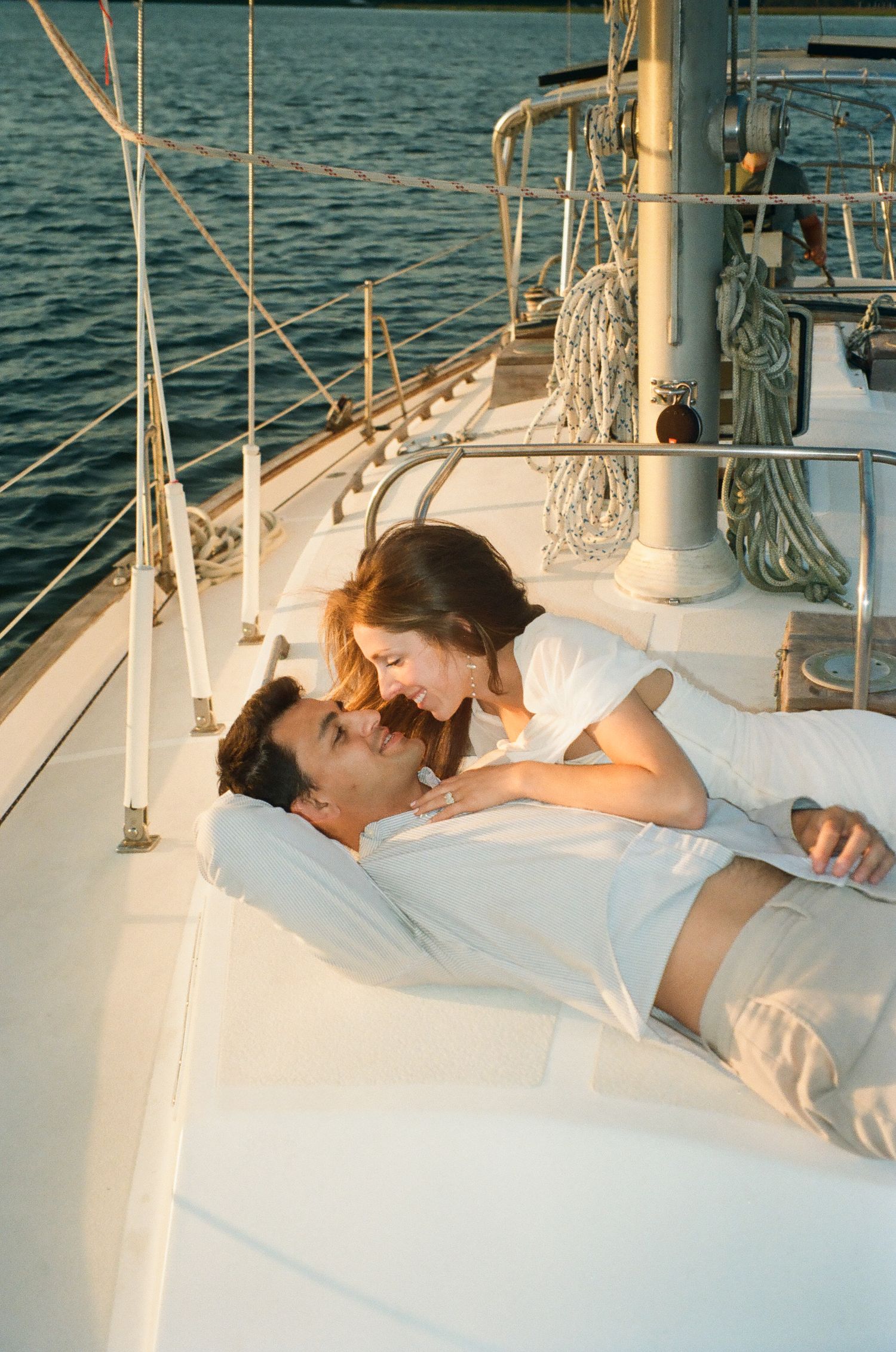 Romantic couple lying together on sailboat deck smiling at each other during golden sunset on the water.