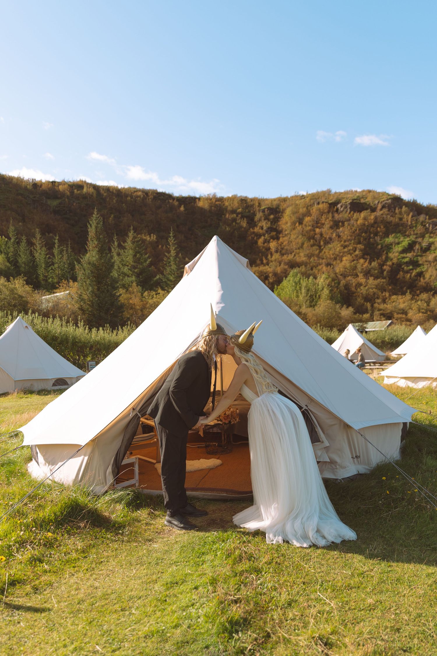 Bride and groom entering a bell tent at a glamping wedding venue with rolling hills and blue sky backdrop.