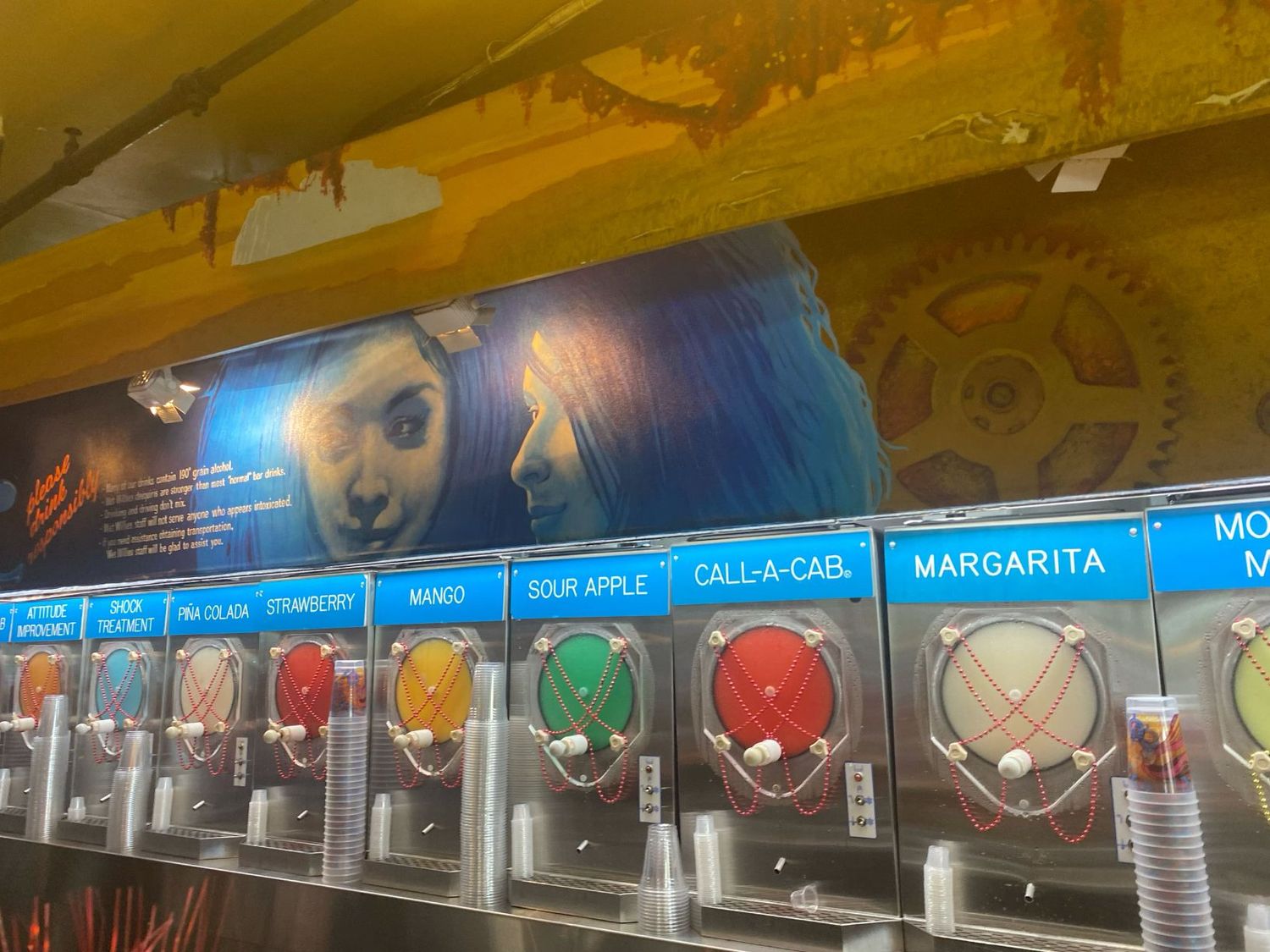 Colorful frozen drink dispensers including margarita and sour apple flavors at a bar.