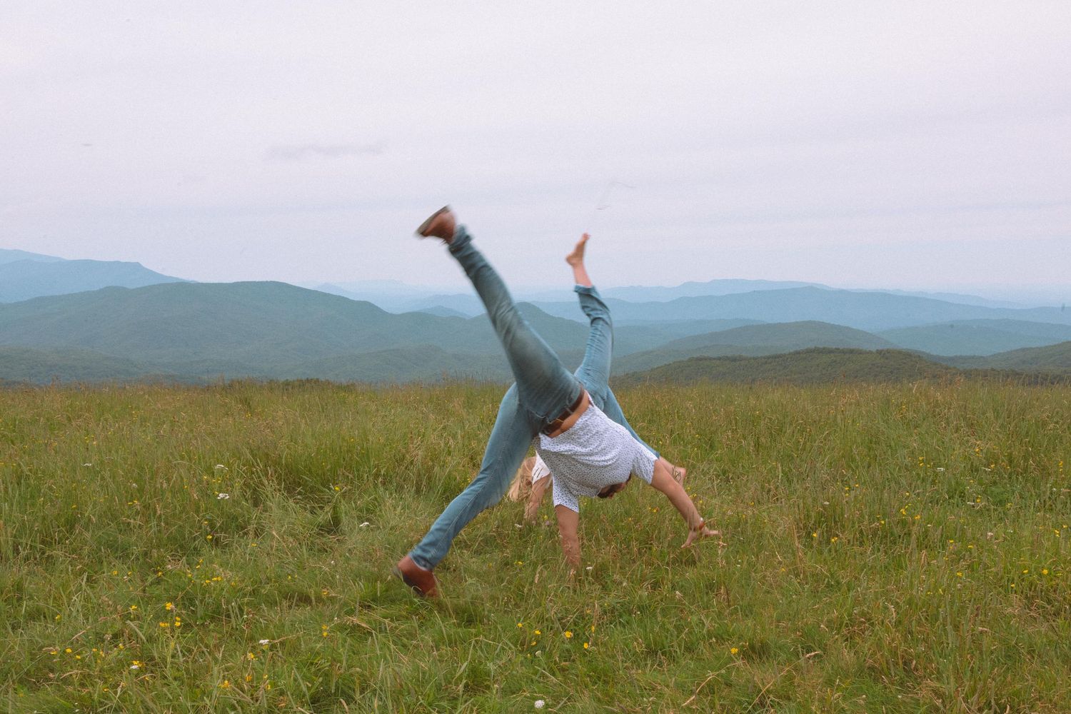 Person doing a cartwheel on a grassy mountain meadow with scenic blue ridge mountain views in the background.