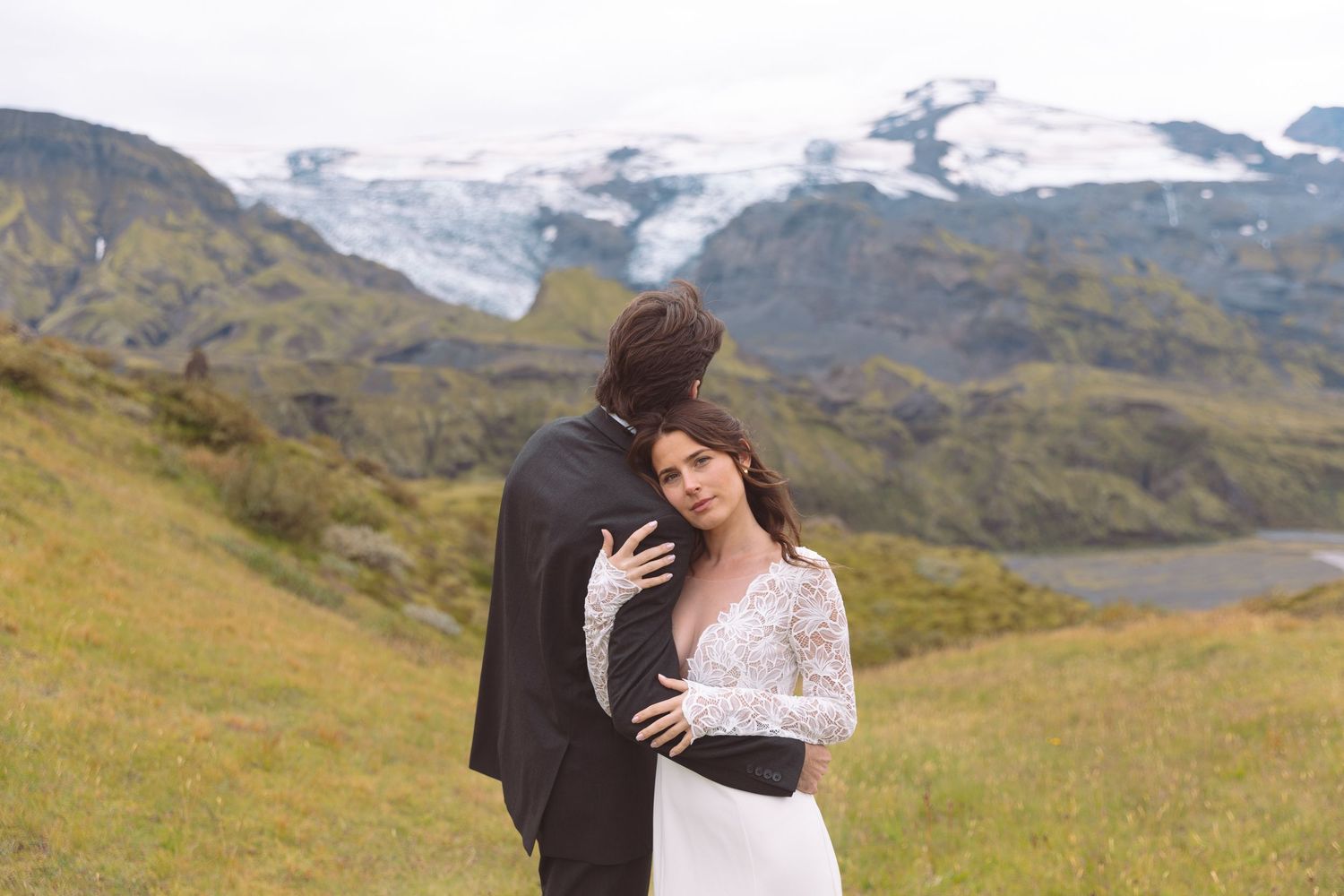 Bride leans into groom while embracing in front of stunning glacial mountain landscape in Iceland.