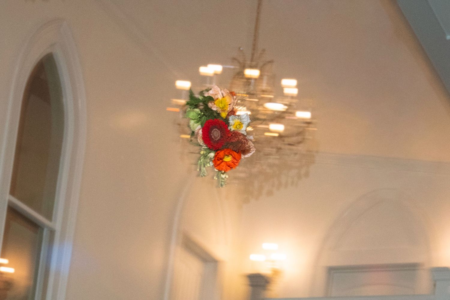 Ornate chandelier adorned with colorful floral arrangement in a white elegant ballroom venue.