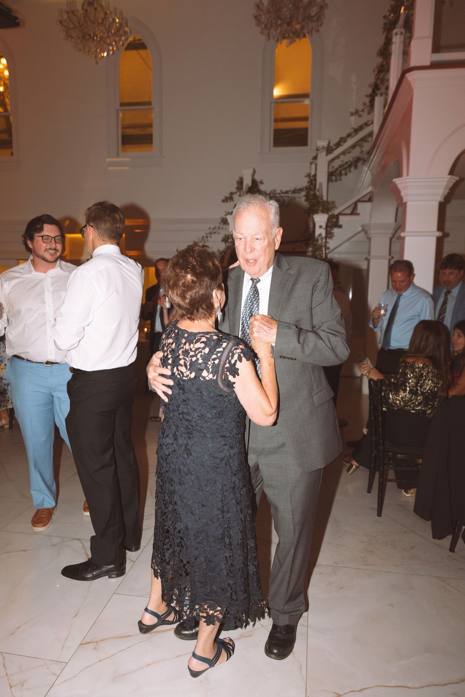 Elderly couple dancing together at a wedding reception in an elegant venue with marble floors.