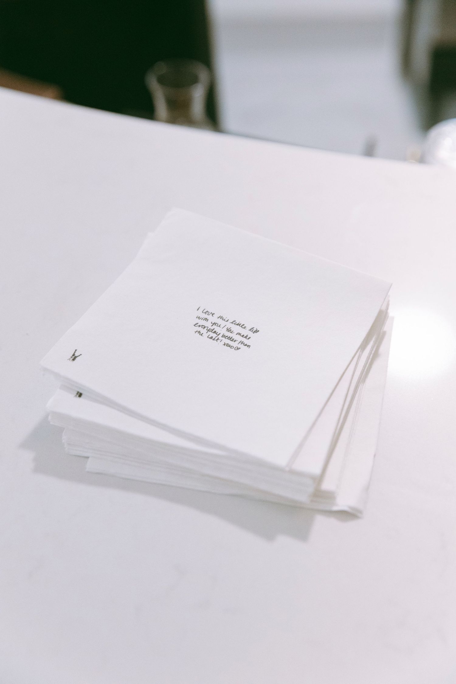 Stack of white papers with handwritten text on top, placed on a white table in a minimalist setting.