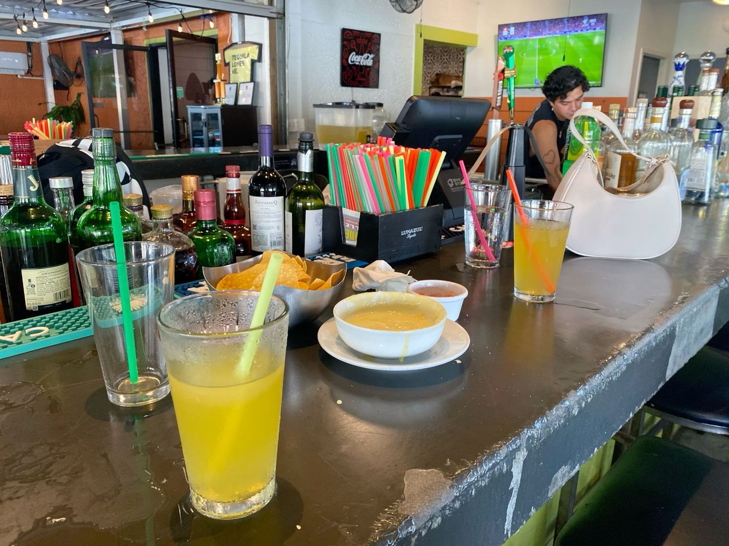Colorful bar counter with orange juice drinks, soup bowl, and snacks at casual restaurant.