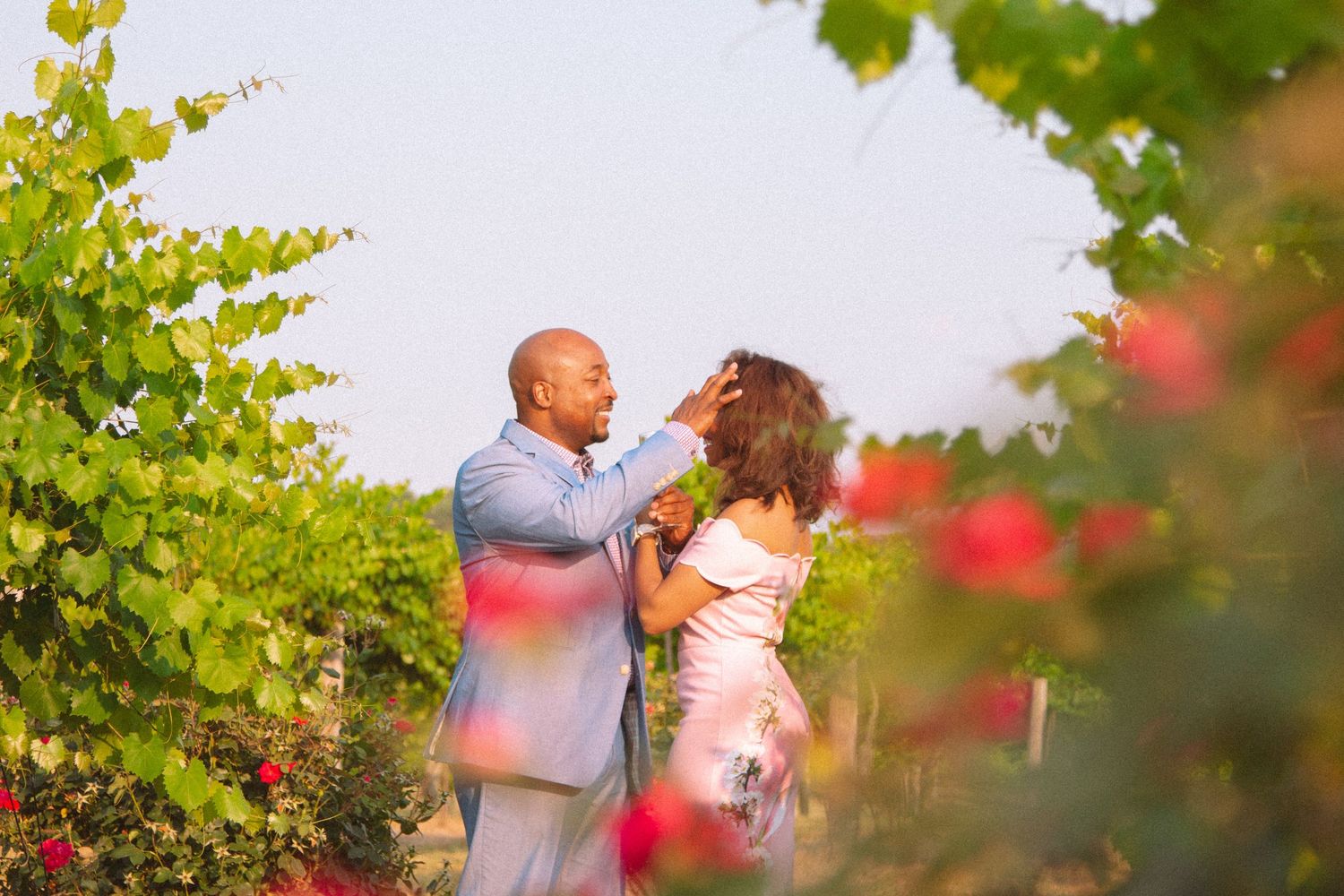 Couple sharing a romantic moment together among colorful roses and green vines in a vineyard.