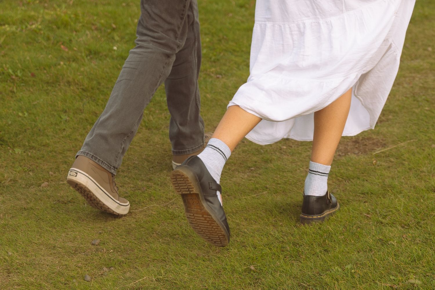 Close-up of a couple walking on green grass, woman in white dress and ankle socks.