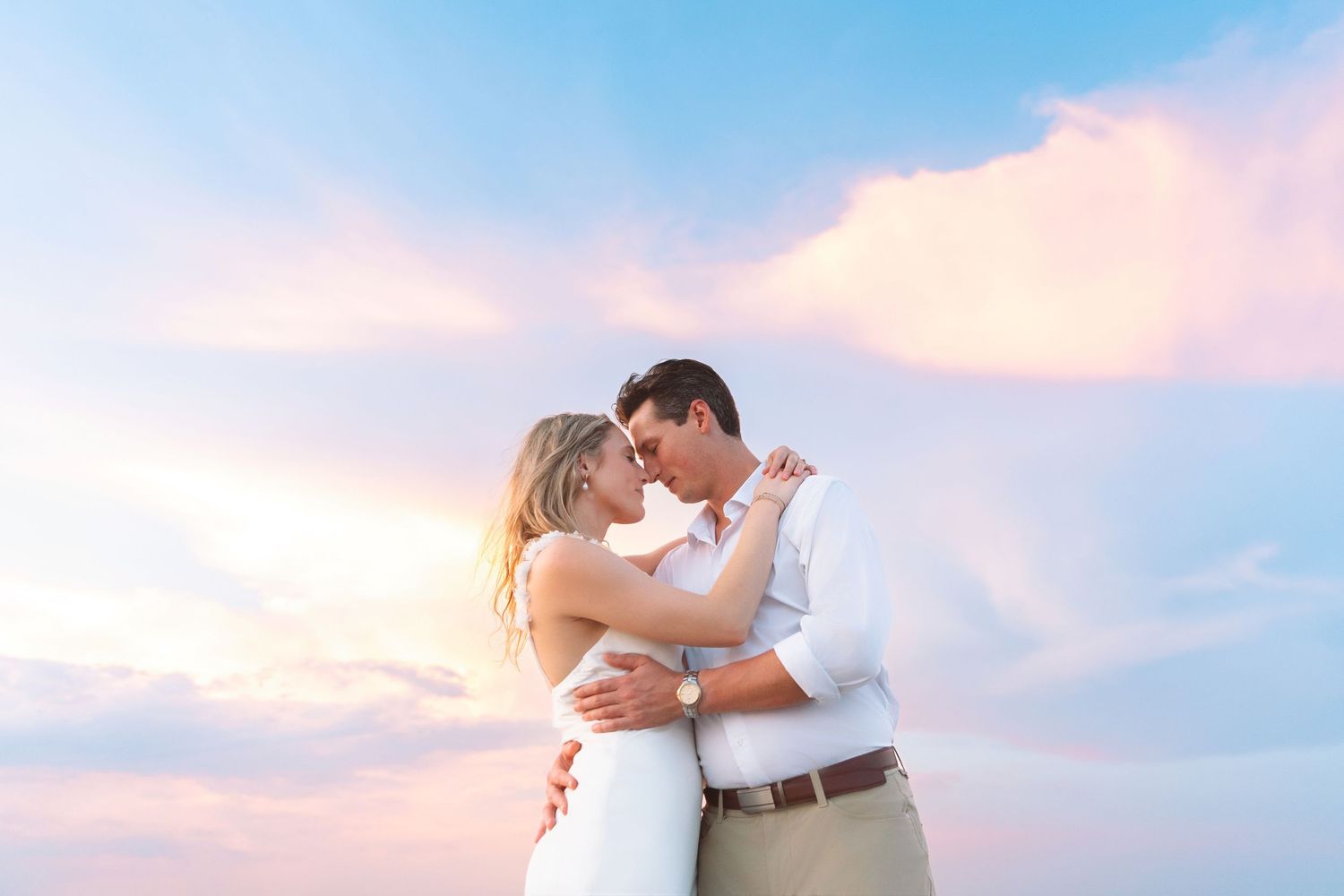 Couple embracing under a stunning pink and blue sunset sky, sharing an intimate moment outdoors.