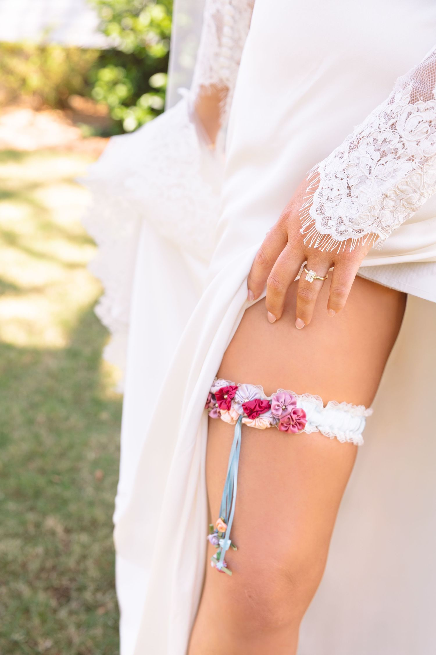 Close-up of bride wearing a floral wedding garter with pink flowers and blue ribbon.