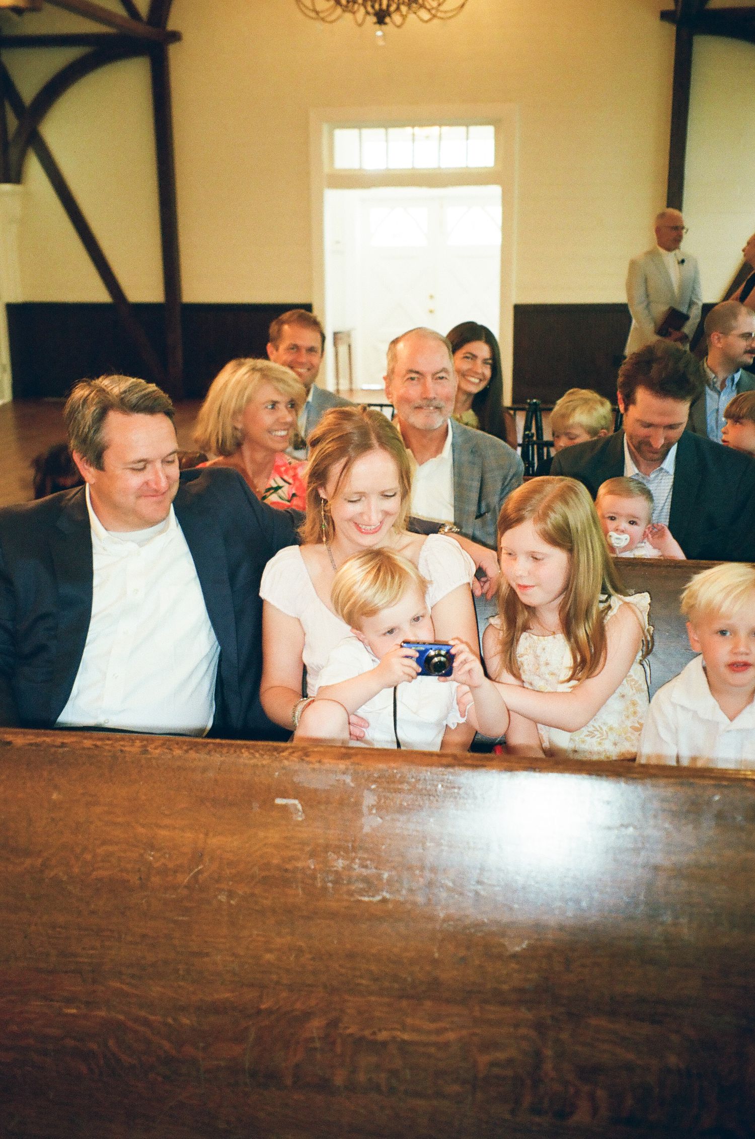 Family gathering in church pew, parents with children viewing camera at wedding or christening ceremony.